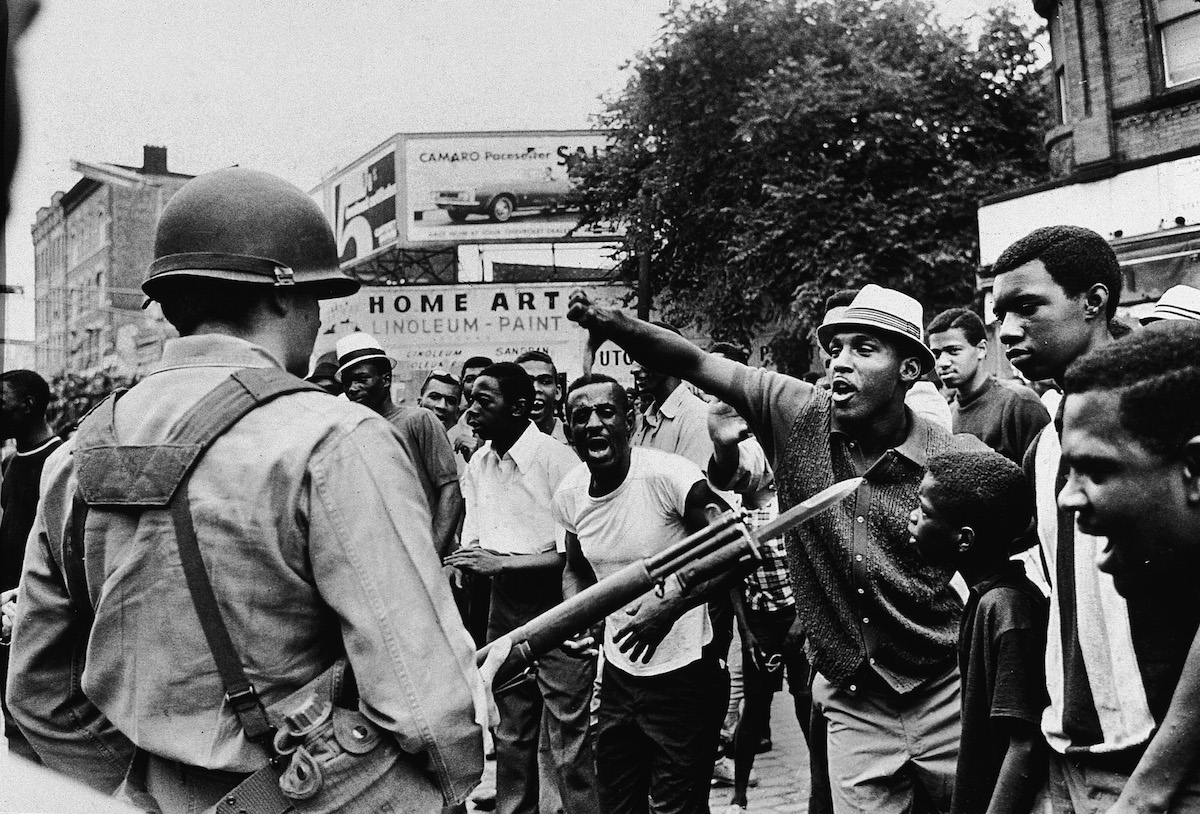 A back man gestures with his thumb down to an armed National Guardsman, during a protest in the Newark race riots, July 14, 1967. (Neal Boenzi—New York Times Co. / Getty Images)