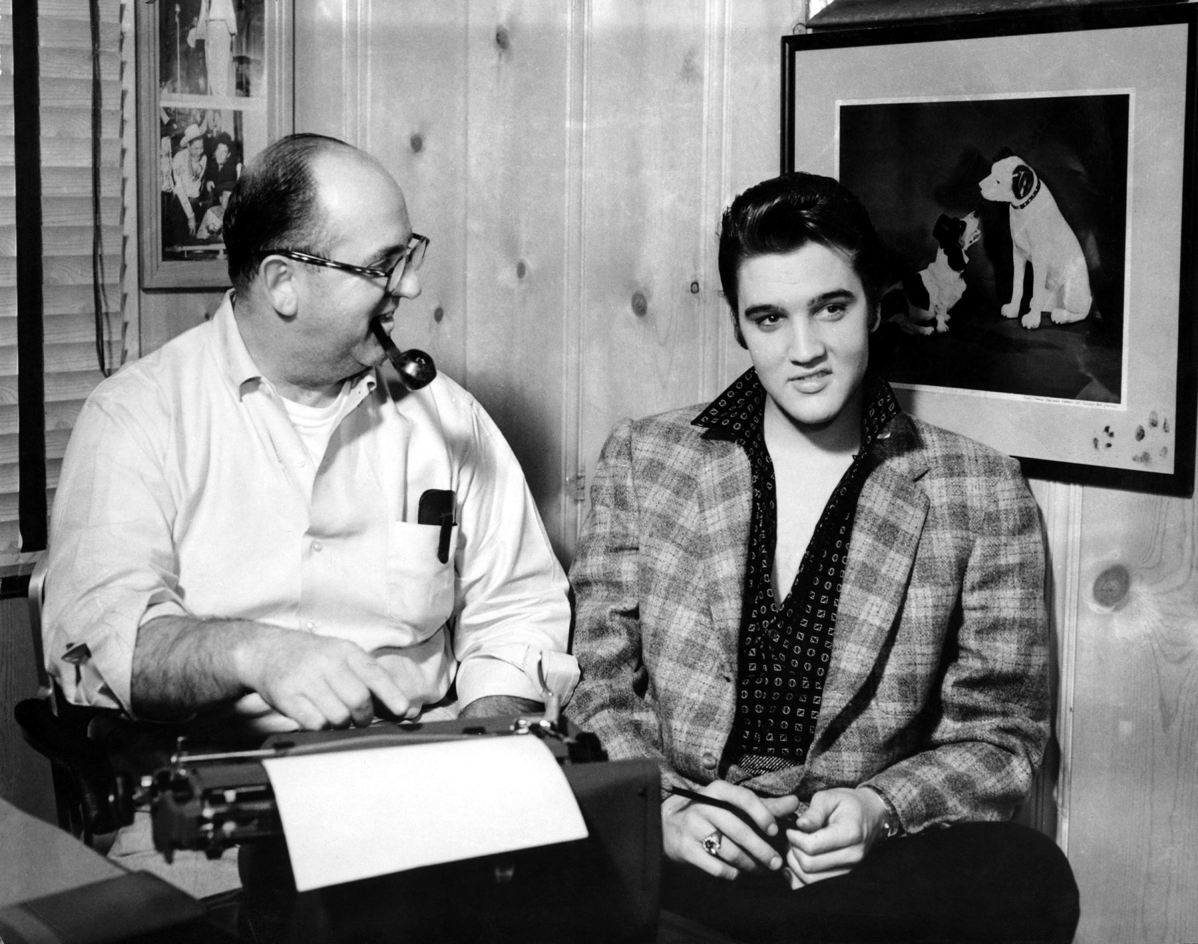 Elvis and his manager Colonel Tom Parker sit at a typewriter in front of the a picture of the RCA Victor Dog in circa 1956 in Memphis, Tennessee.