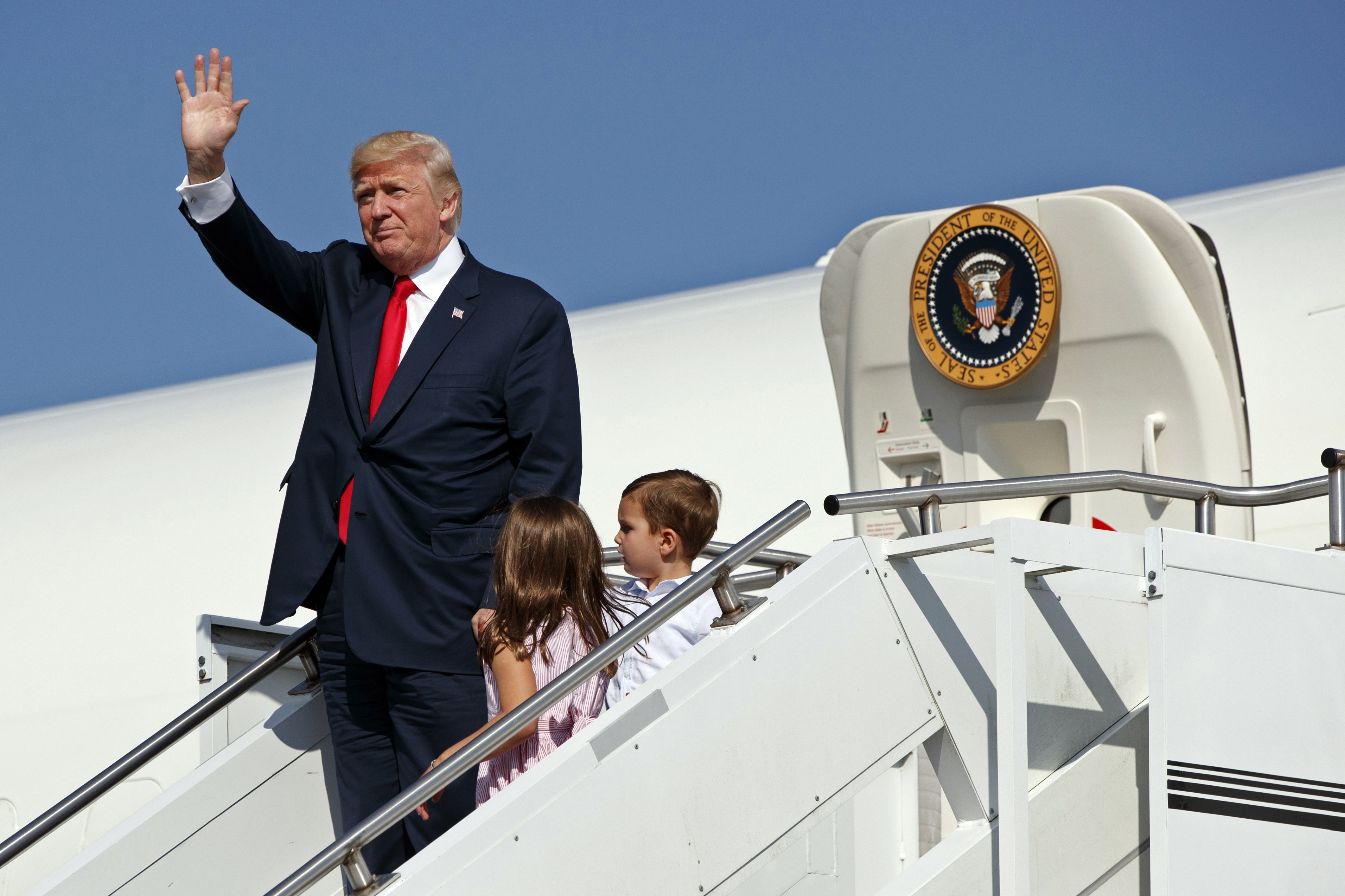 President Donald Trump waves as he walks down the steps of Air Force One with his grandchildren after arriving at Morristown Municipal Airport to begin his summer vacation at his Bedminster golf club in Morristown, N.J. on Aug. 4, 2017. (Evan Vucci—AP)