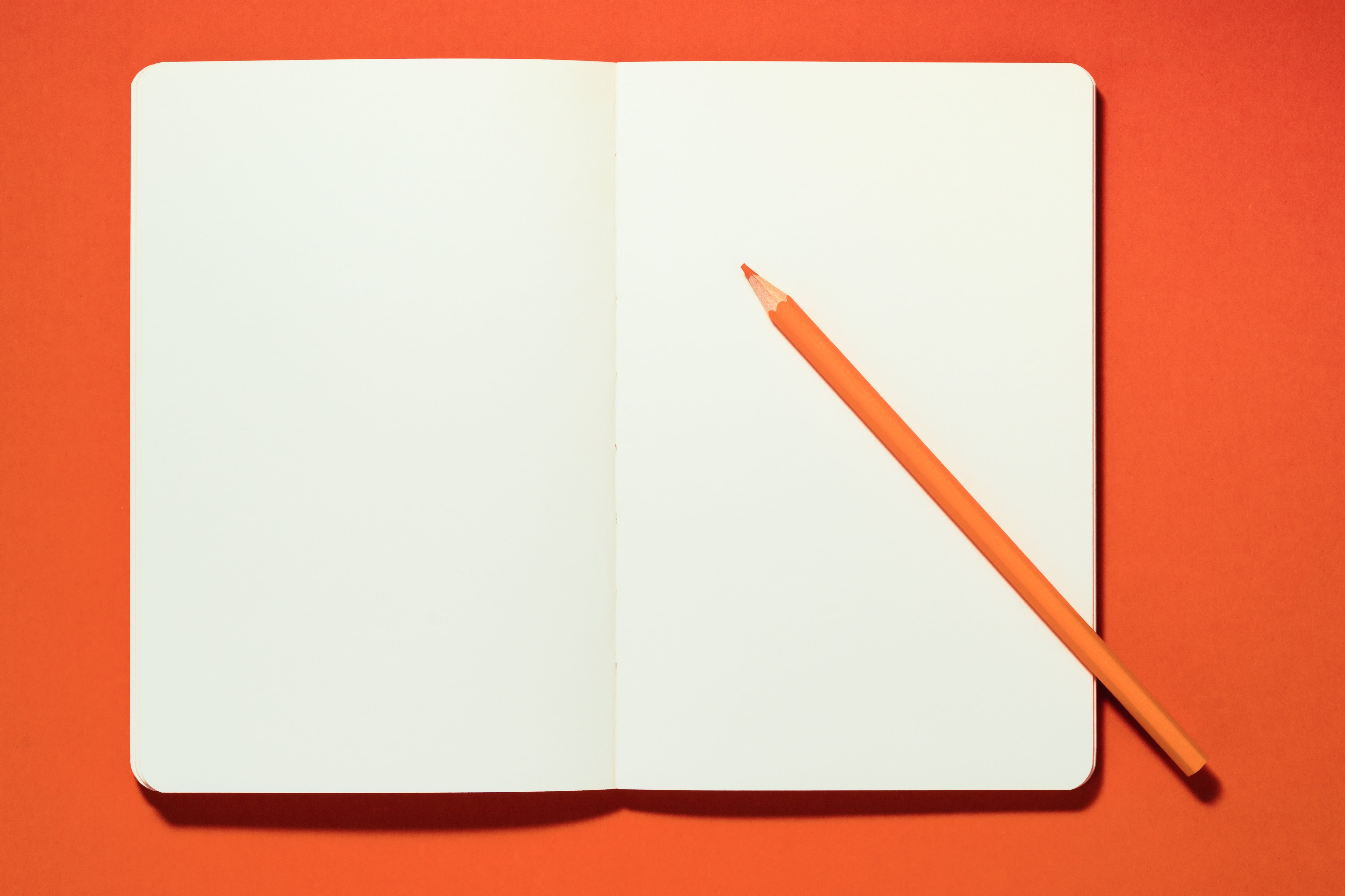 Orange Pencil on a Opened Blank Notebook against Orange Color Background Overhead View. (Getty Images)