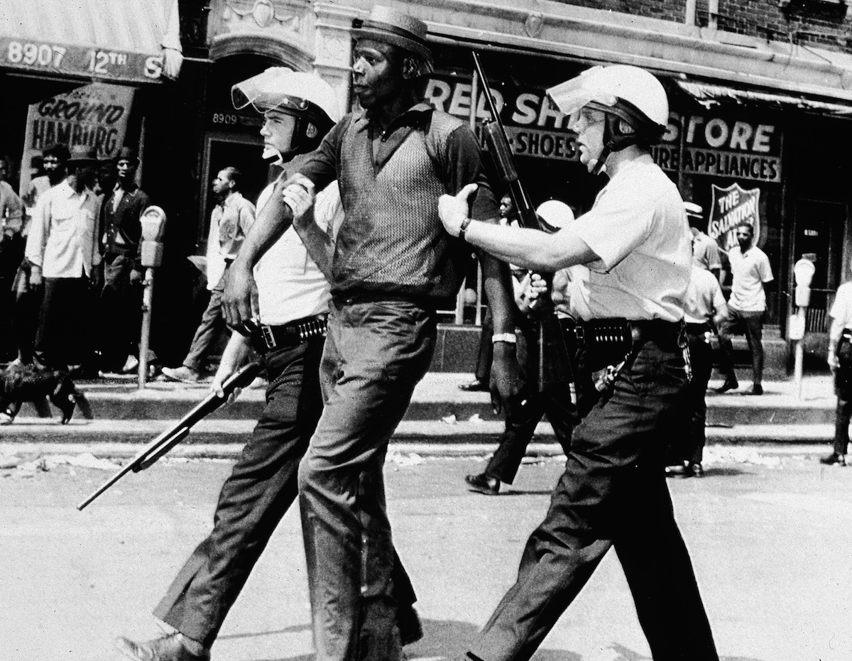 Two police officers in full riot gear arrest a man during a breakout of rioting and looting on the West side of Detroit on July 23, 1967 (American Stock / Getty Images)