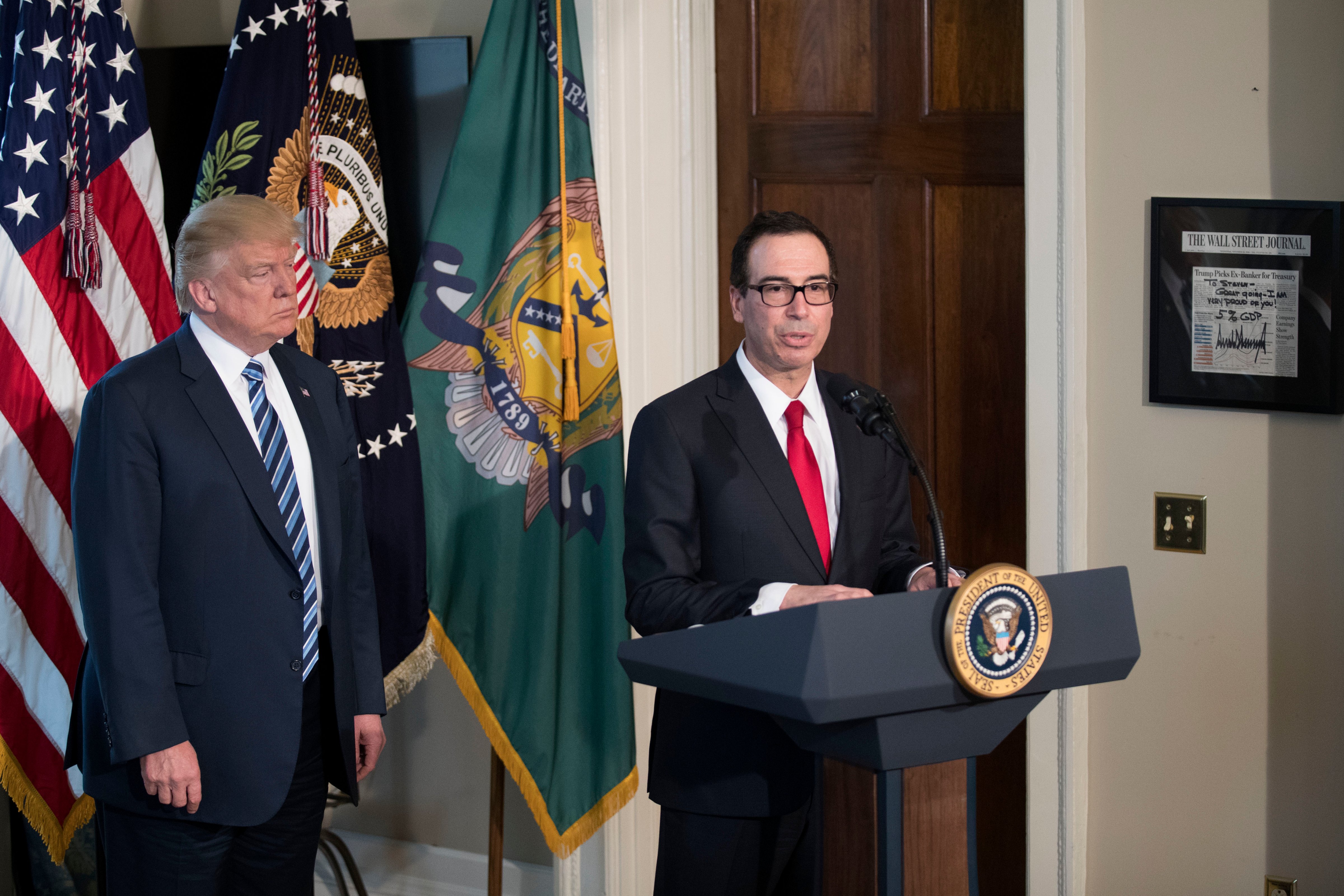 U.S. President Donald Trump (L) listens as Secretary of Treasury Steven Mnuchin (R) delivers remarks in the US Treasury Department building. (Photograph by Shawn Thew—Pool/Getty)