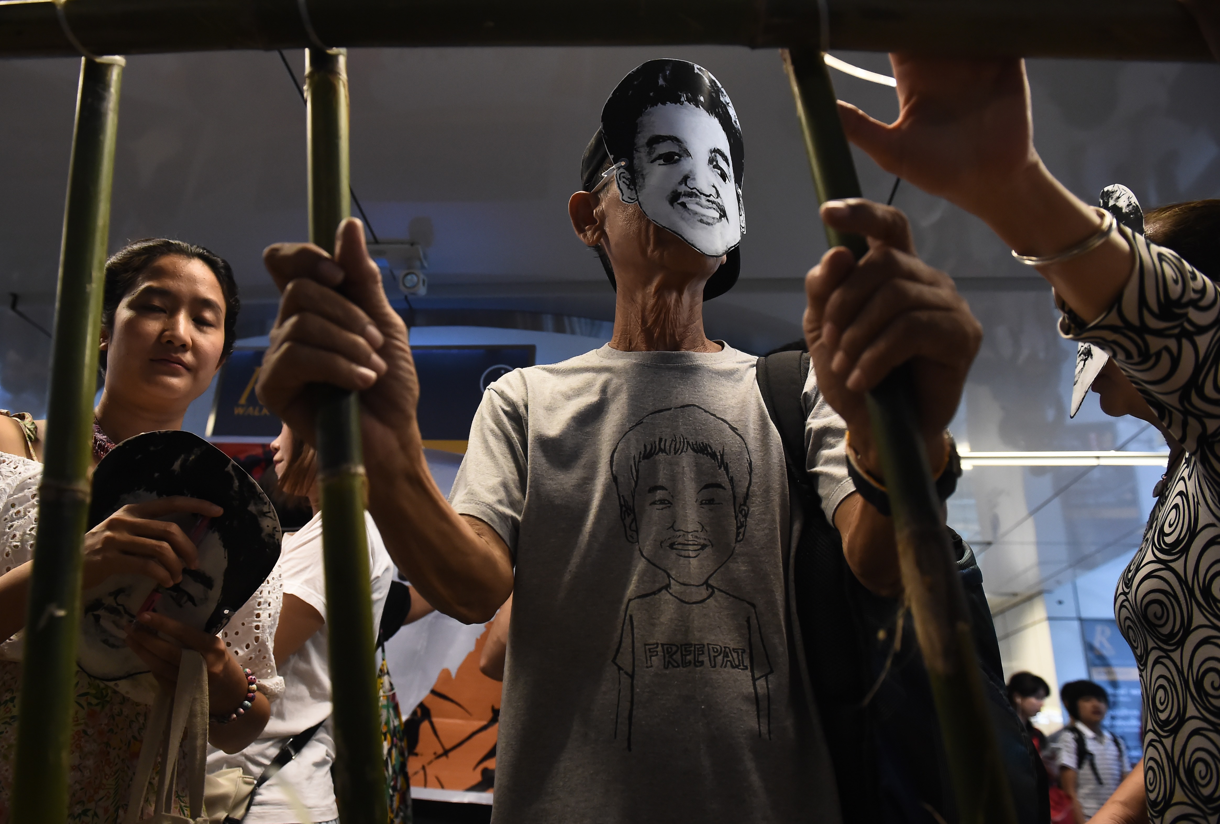People stand behind makeshift bars wearing masks of Thai human rights activist Jatupat Pai Boonpattararaksa in Bangkok on June 22, 2017. (Lillian Suwanrumpha—AFP/Getty Images)