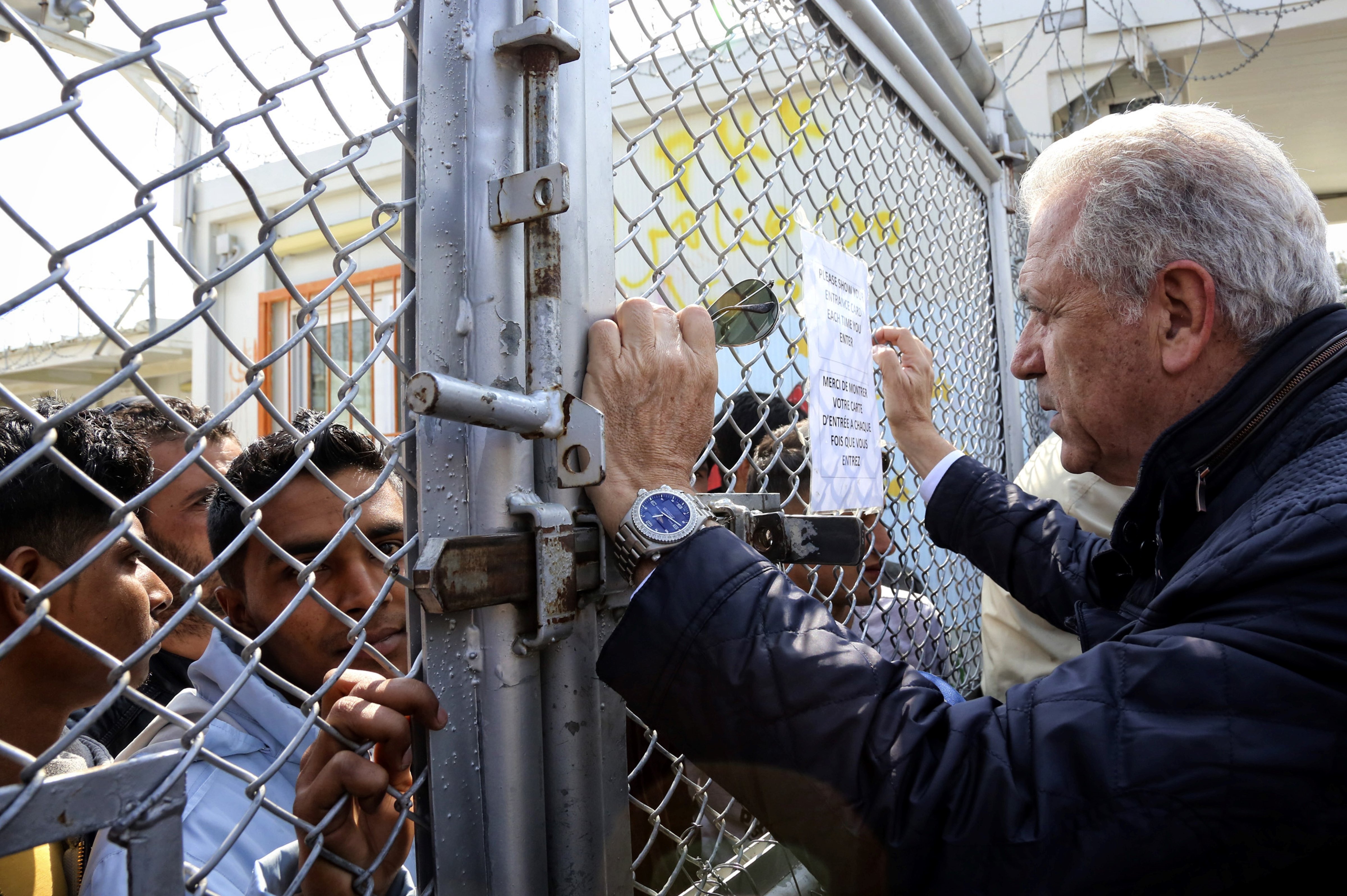 E.U. Migration Commissioner Dimitris Avramopoulos talks with migrants  during his visit to the  Moria migrant camp on March 16, 2017 on the island of Lesbos, almost a year after an EU-Turkey deal.
