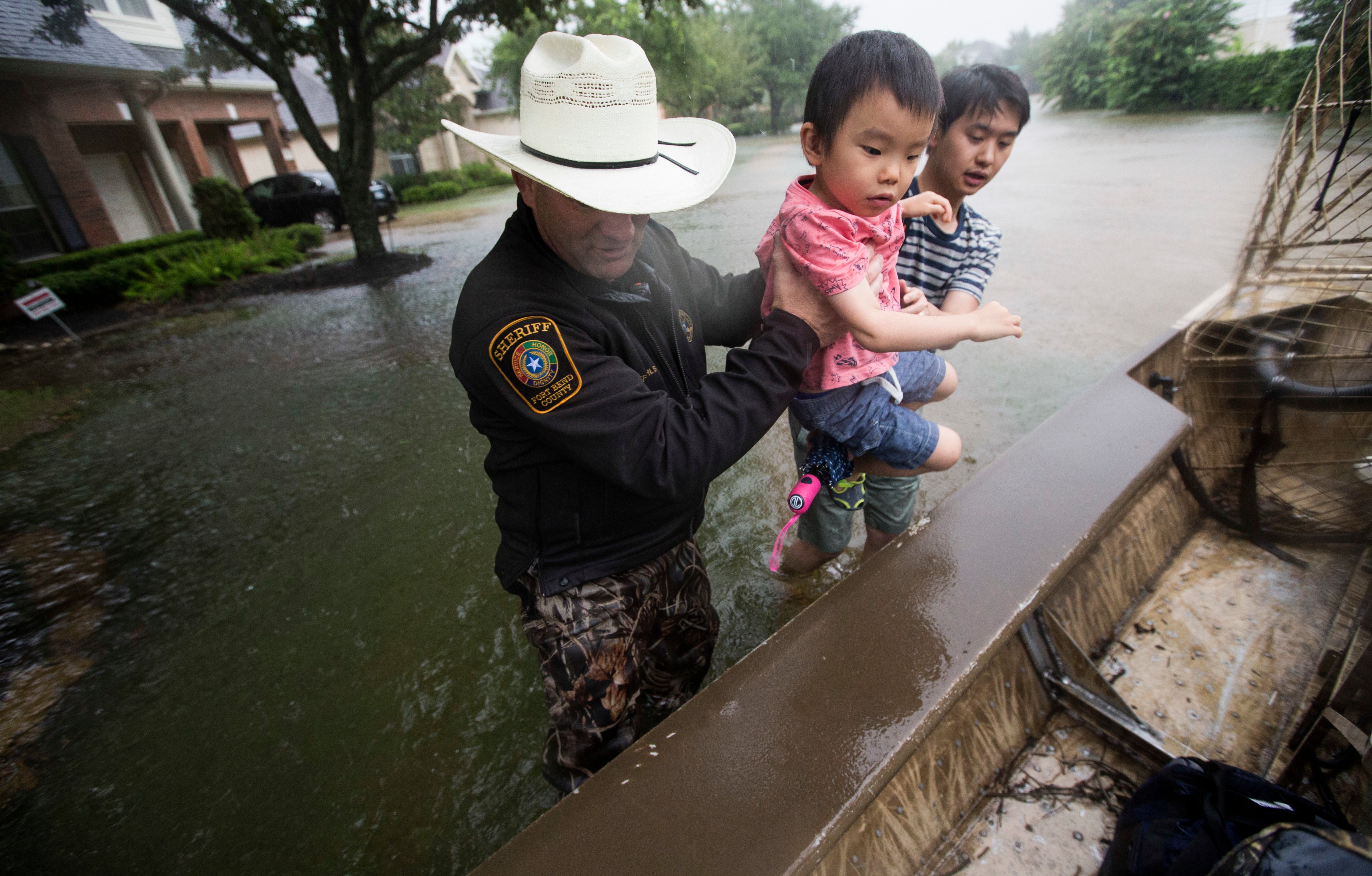Fort Bend County Sheriff Troy Nehls and Lucas Wu lift Ethan Wu into an airboat as they are evacuated from rising waters from Tropical Storm Harvey, at the Orchard Lakes subdivision on Sunday, Aug. 27, 2017, in unincorporated Fort Bend County, Texas. (Brett Coomer&mdash;AP)