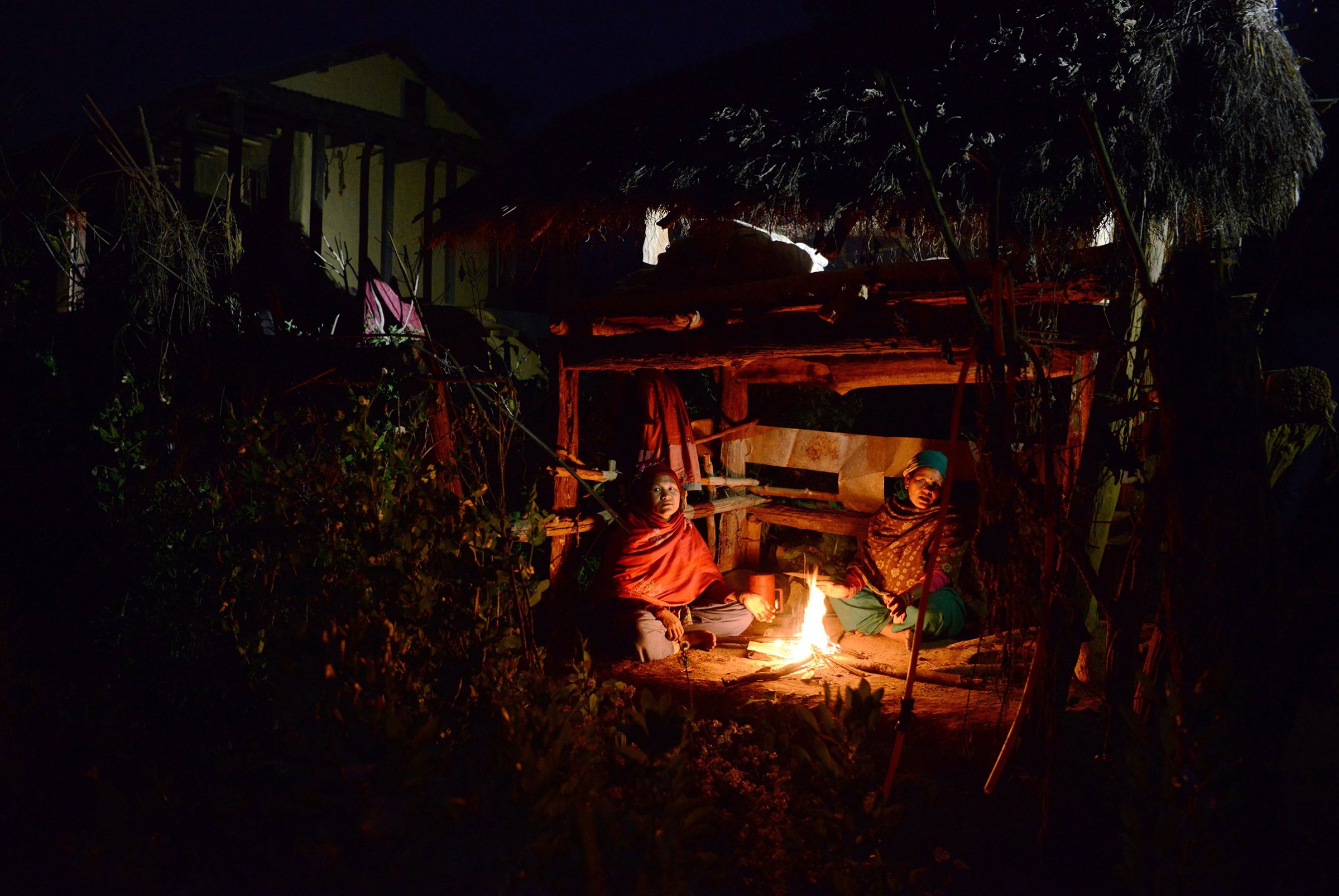 Nepalese women Pabitra Giri (L) and Yum Kumari Giri (R) sit by a fire as they live in a Chhaupadi hut during their menstruation period in Surkhet District, some 520km west of Kathmandu on Feb. 3, 2017.