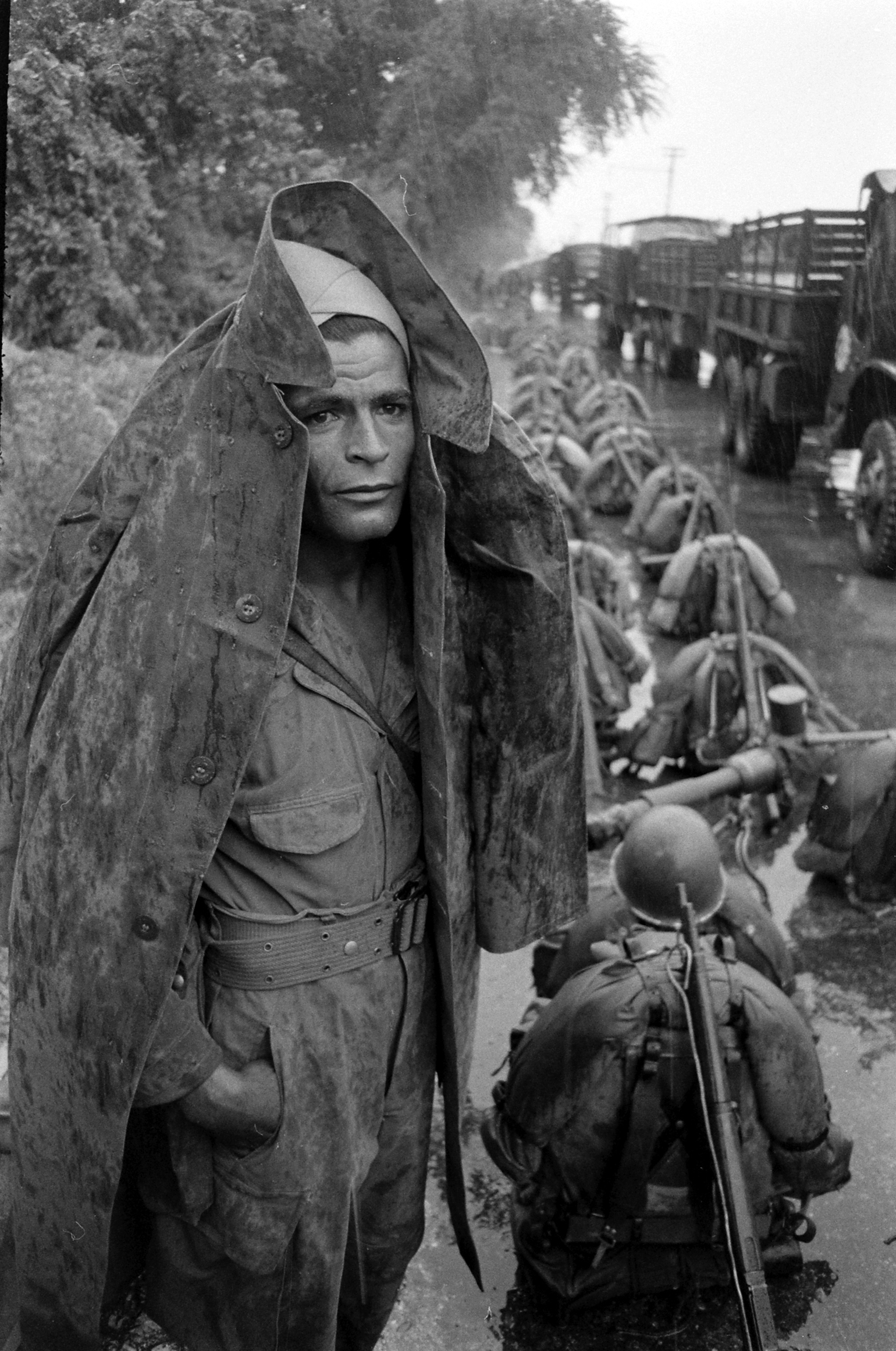 A soldier stands beside a line of packs in the rain, Hanoi, Vietnam, October 1954.