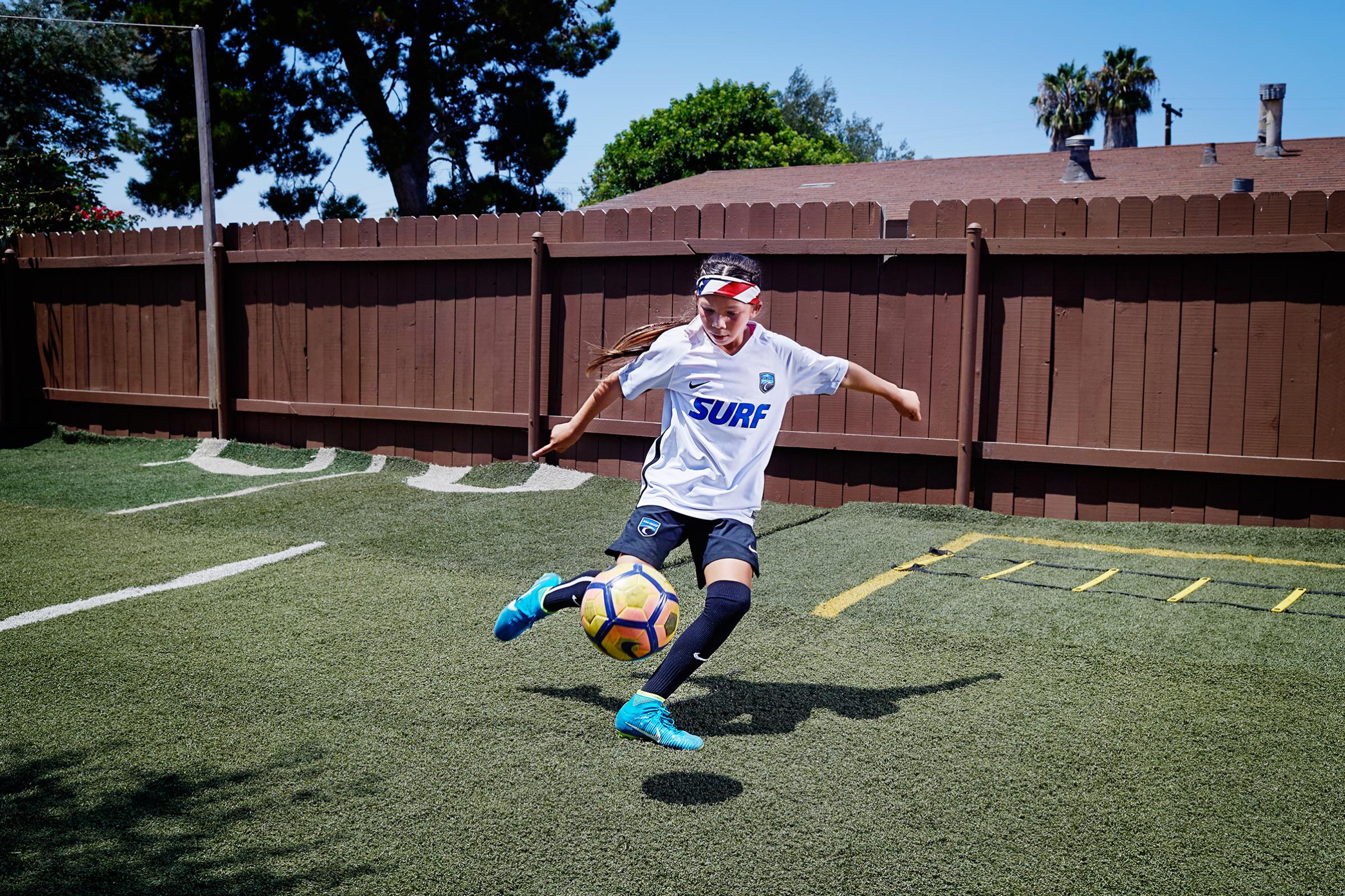 Melanie Barcenas, 9, practicing in her San Diego backyard, hopes to follow in the footsteps of the superstar Neymar. “He plays just like me,” she says. Melanie plays multiple soccer games most weekends. To save money, her family stays in a hotel only if a game is more than a four-hour drive from home. Here Melanie is photographed at home where her father Carlos made a practice field for her in their backyard, on Aug. 3, 2017.