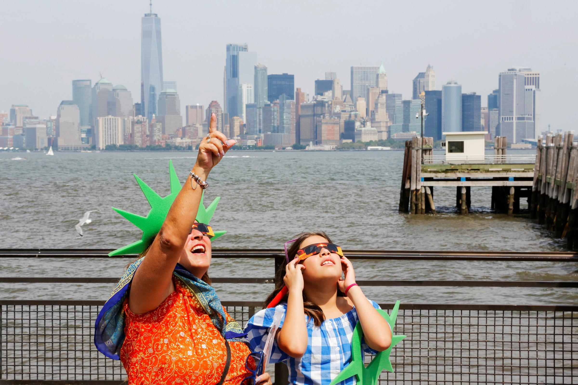 People view the solar eclipse at Liberty State Island as the Lower Manhattan and One World Trade center are seen in the background in New York
