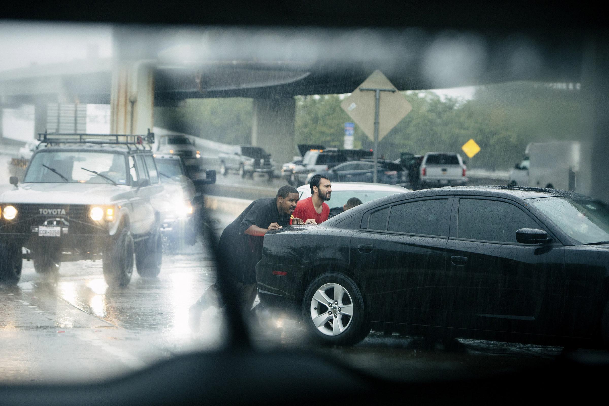 A stalled car gets a push amid heavy rain on a section of Interstate 610 in Houston, Aug. 27, 2017.