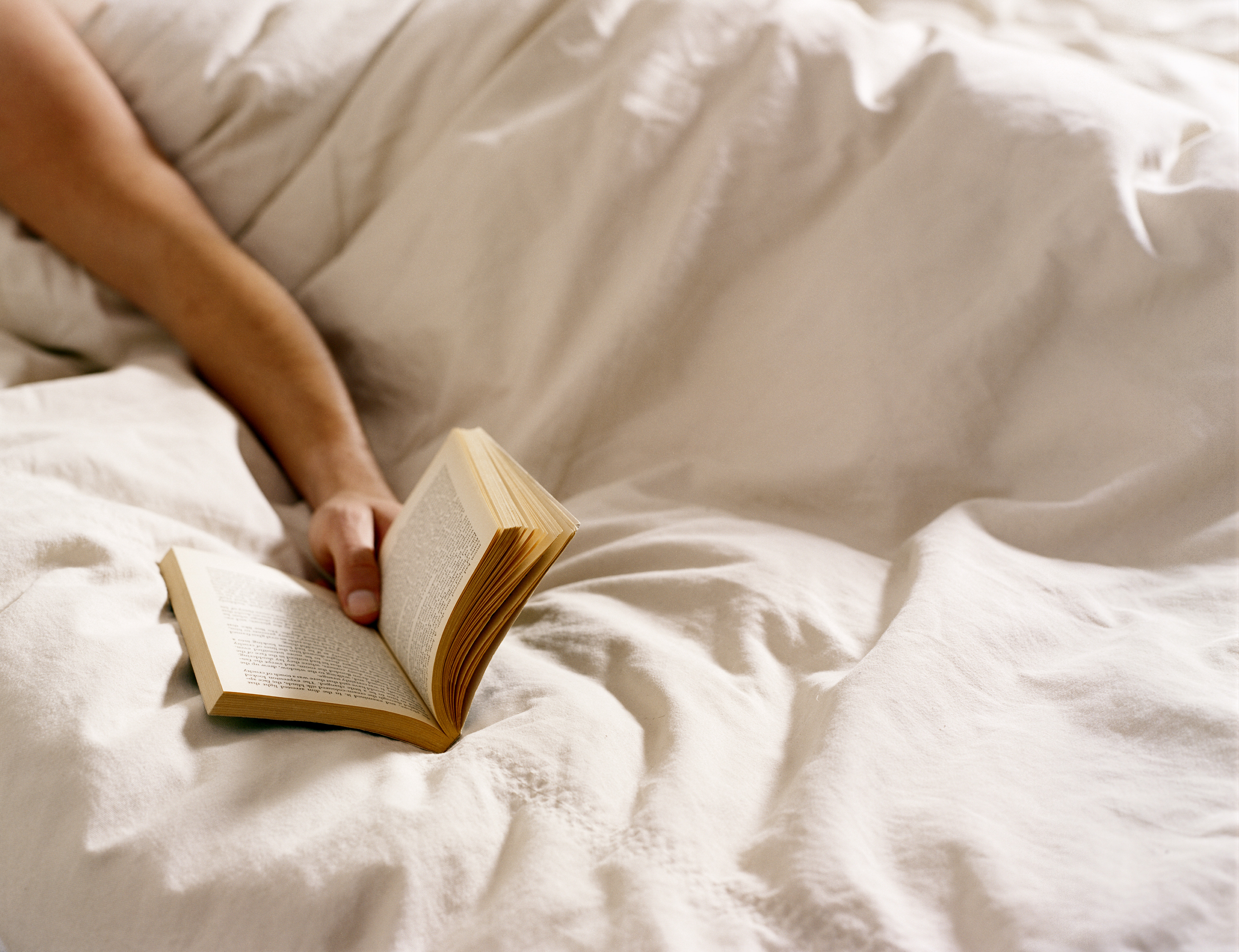 Young man holding open book on bed, close-up (DTP—Getty Images)