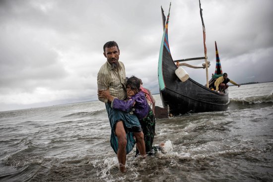 A Rohingya man helps an elderly woman reach the Bangladeshi shore from the boat in which they escaped Myanmar