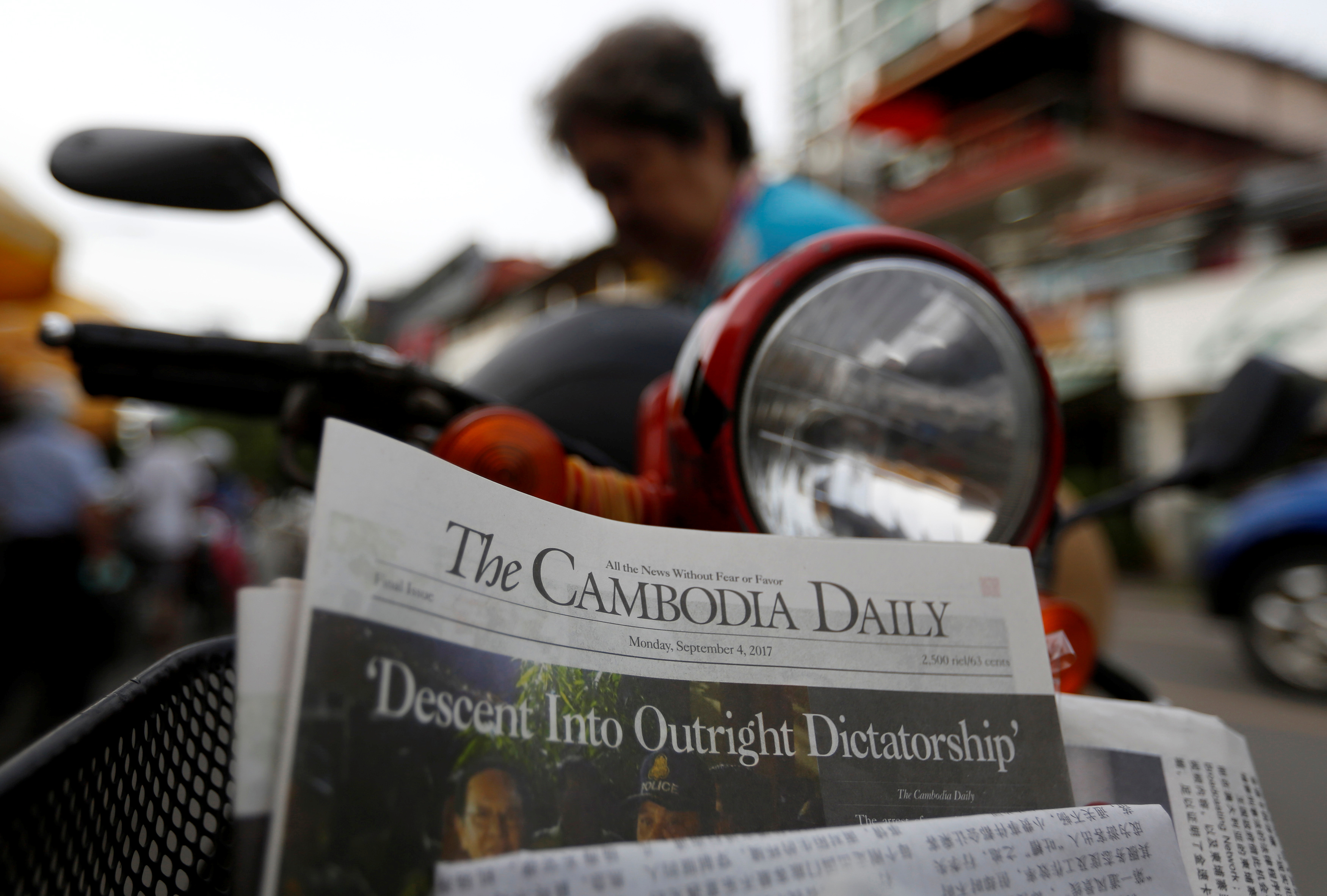 A woman buys the final issue of The Cambodia Daily newspaper at a store along a street in Phnom Penh