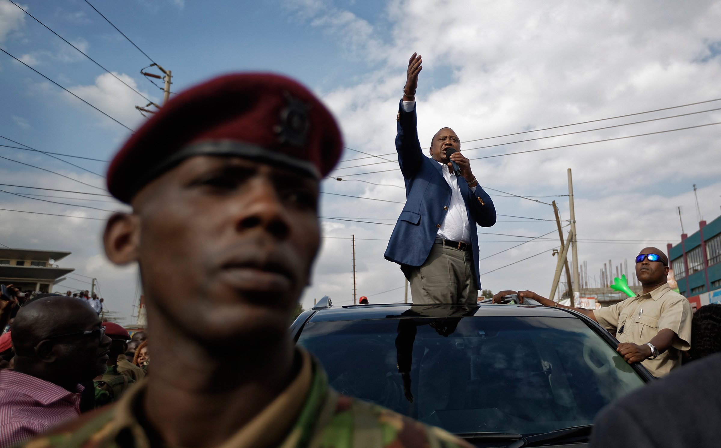 Kenya's President Uhuru Kenyatta, standing through the sunroof of the presidential vehicle, addresses his supporters as a presidential guard provides security, left, on a street in Ongata Rongai, on the outskirts of Nairobi, Kenya, Sept. 5, 2017. Kenya faces an Oct. 17 vote after the Supreme Court nullified Kenyatta's re-election but opposition leader Raila Odinga said Tuesday he does not accept the date, demanding reforms to the electoral commission and other "legal and constitutional guarantees."