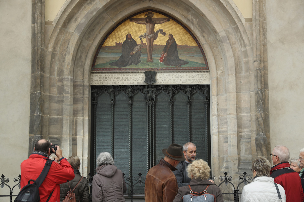 In 2016, visitors stand in front of the cast metal reproduction of Martin Luther's 95 theses in the doorway where in 1517 Luther originally nailed his theses at the Schlosskirche church in Wittenberg, Germany (Sean Gallup—Getty Images)