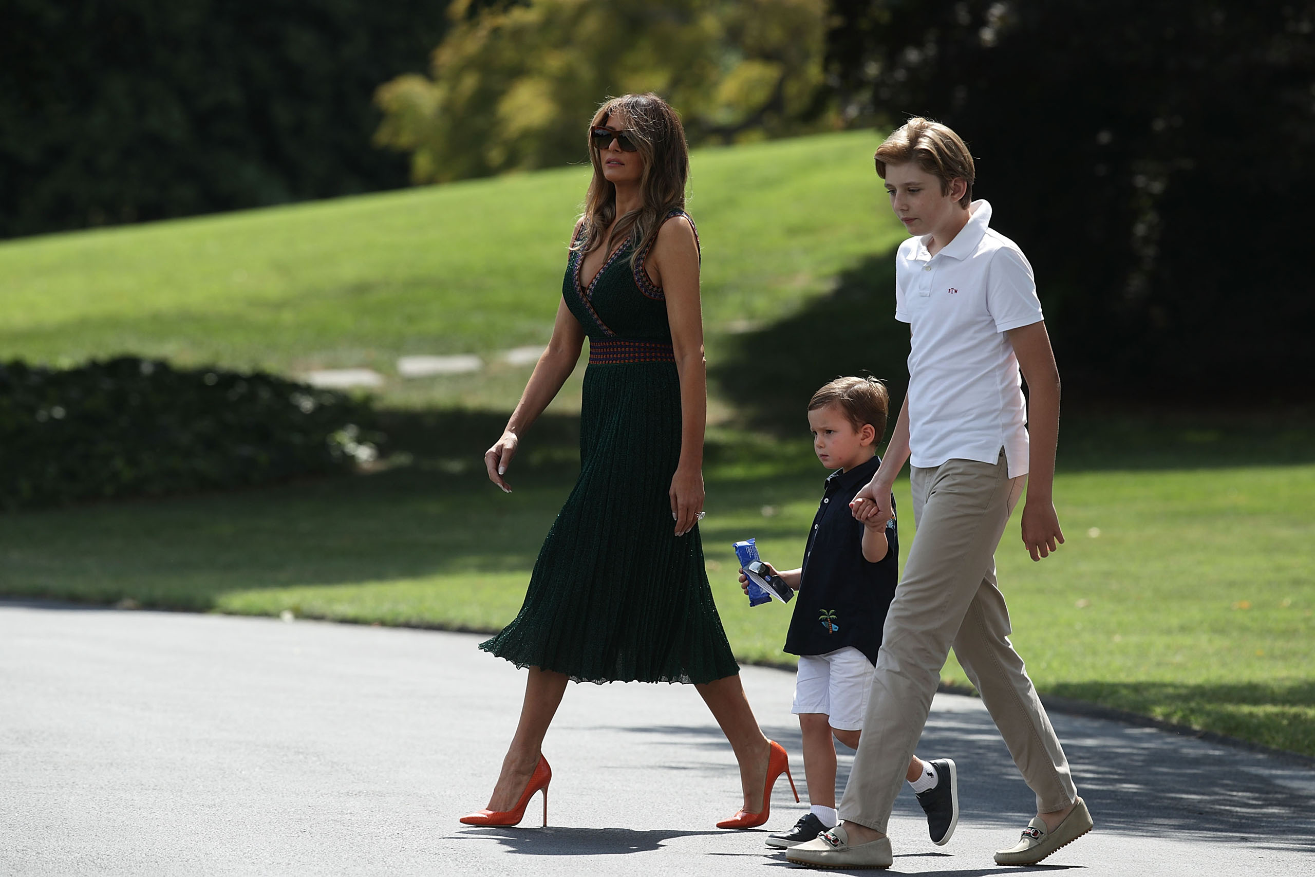 First lady Melania Trump (L), wearing a green Missoni knit dress and orange Manolo Blahnik stilettos, walks with son Barron (R), and grandson Joseph Frederick Kushner (2nd L) towards the Marine One on the South Lawn of the White House prior to a departure Aug. 25, 2017.