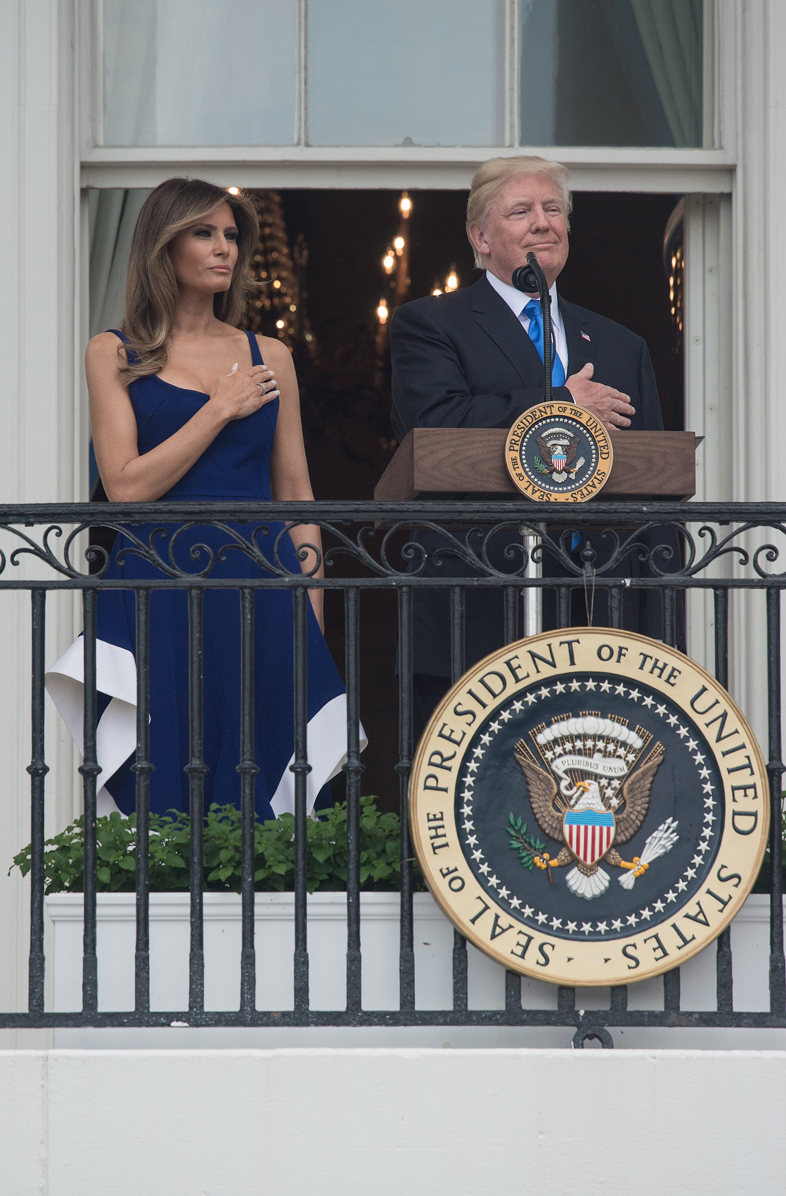 President Donald Trump and first lady Melania Trump, wearing a blue and white dress by designer Esteban Cortázar, listen to the national anthem during the military families picnic at the White House in Washington, DC, on July 4, 201