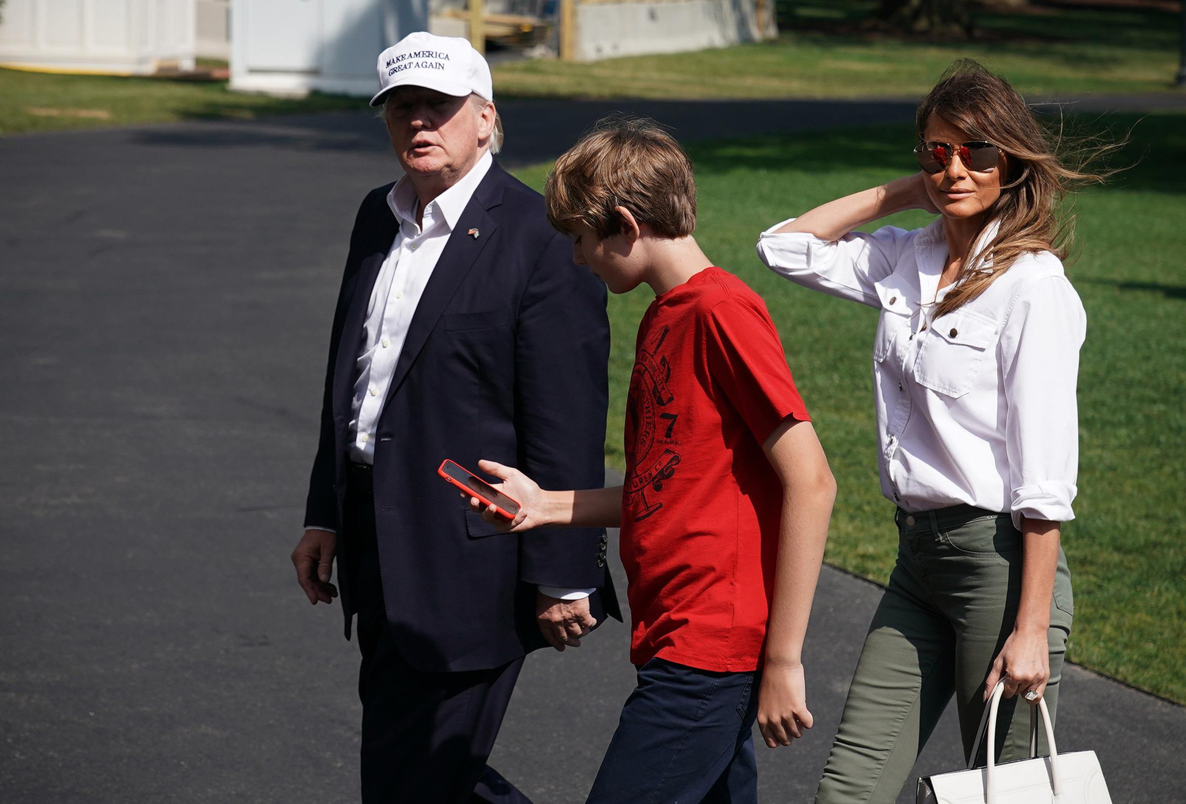 President Donald Trump, First Lady Melania Trump wearing a white button-up top and olive green J Brand pants, and their son Barron walk across the South Lawn upon return to the White House on June 18, 2017.