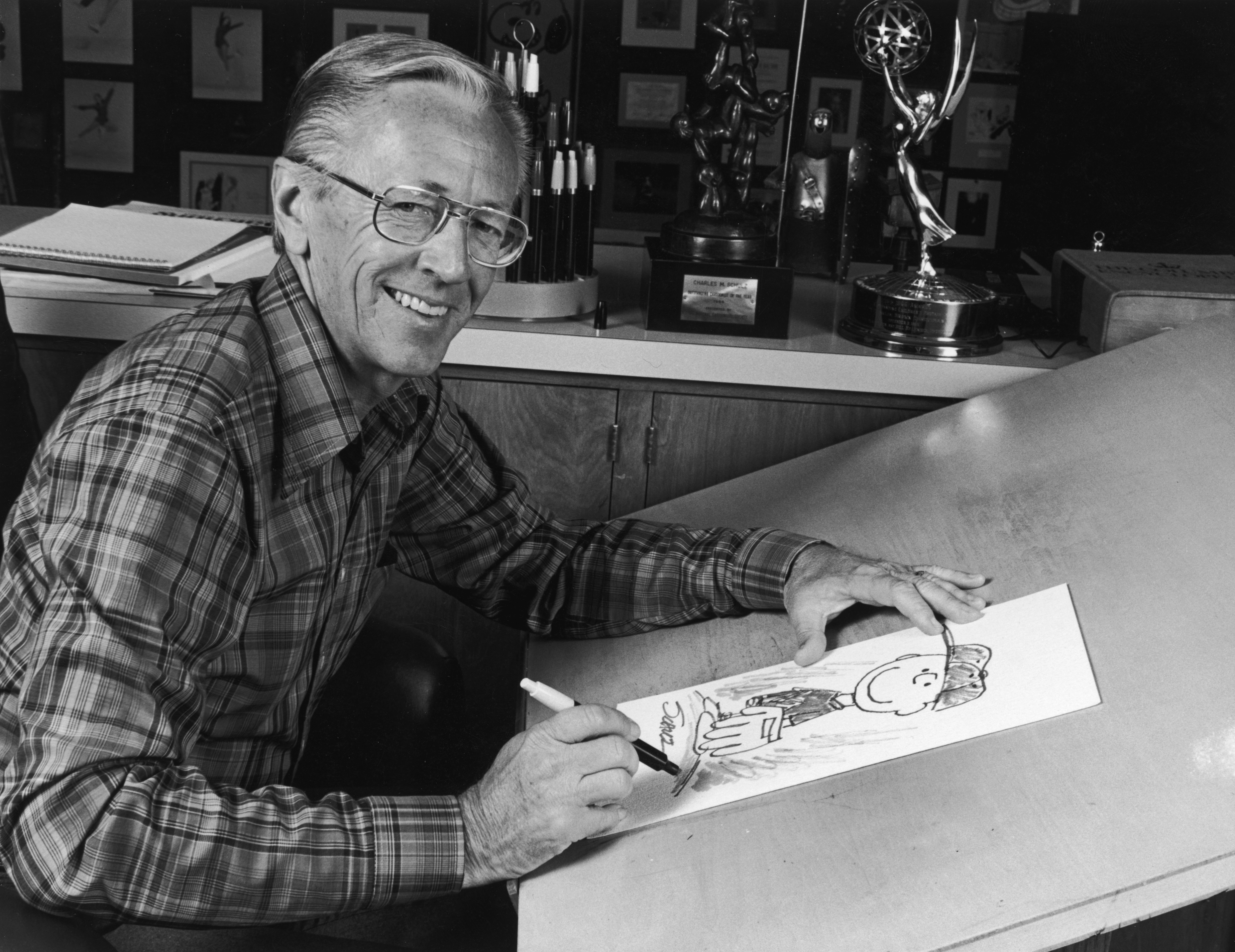 Portrait of American cartoonist Charles M Schulz (1922 - 2001), creator of the 'Peanuts' comic strip, sitting at his studio drawing table with a picture of his character Charlie Brown and some awards behind him. (CBS Photo Archive—Getty Images)