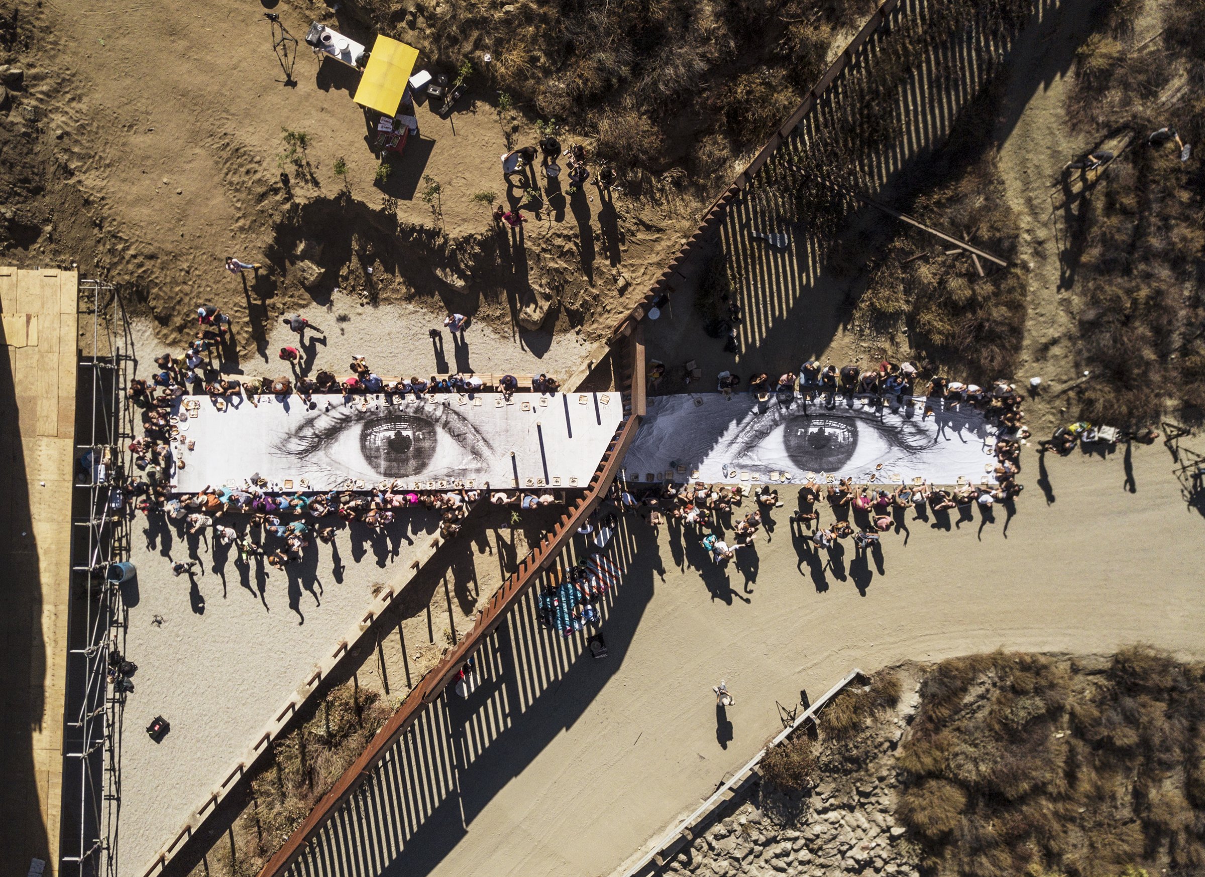 A picnic takes place on JR’s Giant Picnic, a photograph of the eyes of a Dreamer at the U.S.-Mexico border in Tecate, Mexico, on Oct. 8