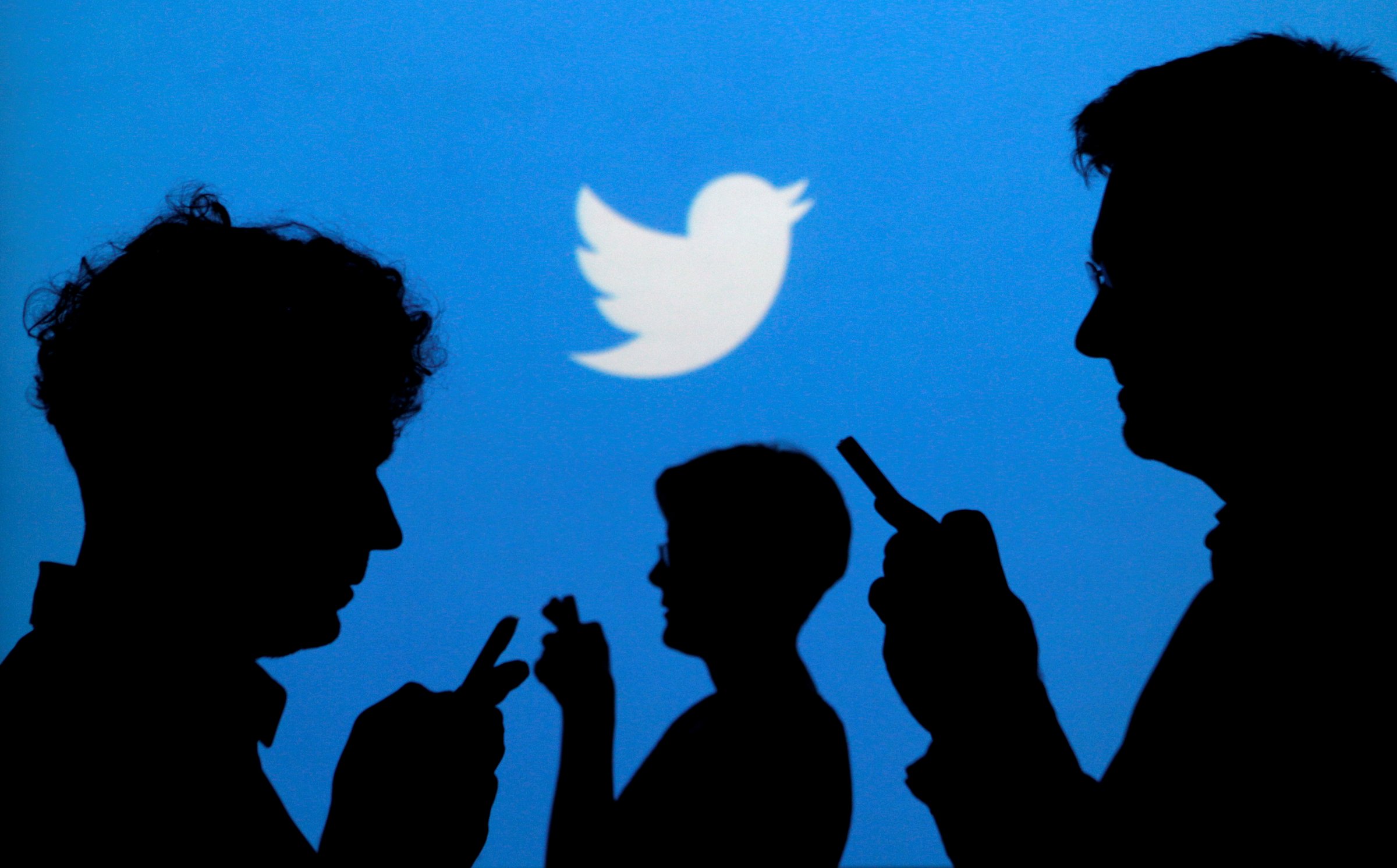 FILE PHOTO -  People holding mobile phones are silhouetted against a backdrop projected with the Twitter logo  in Warsaw