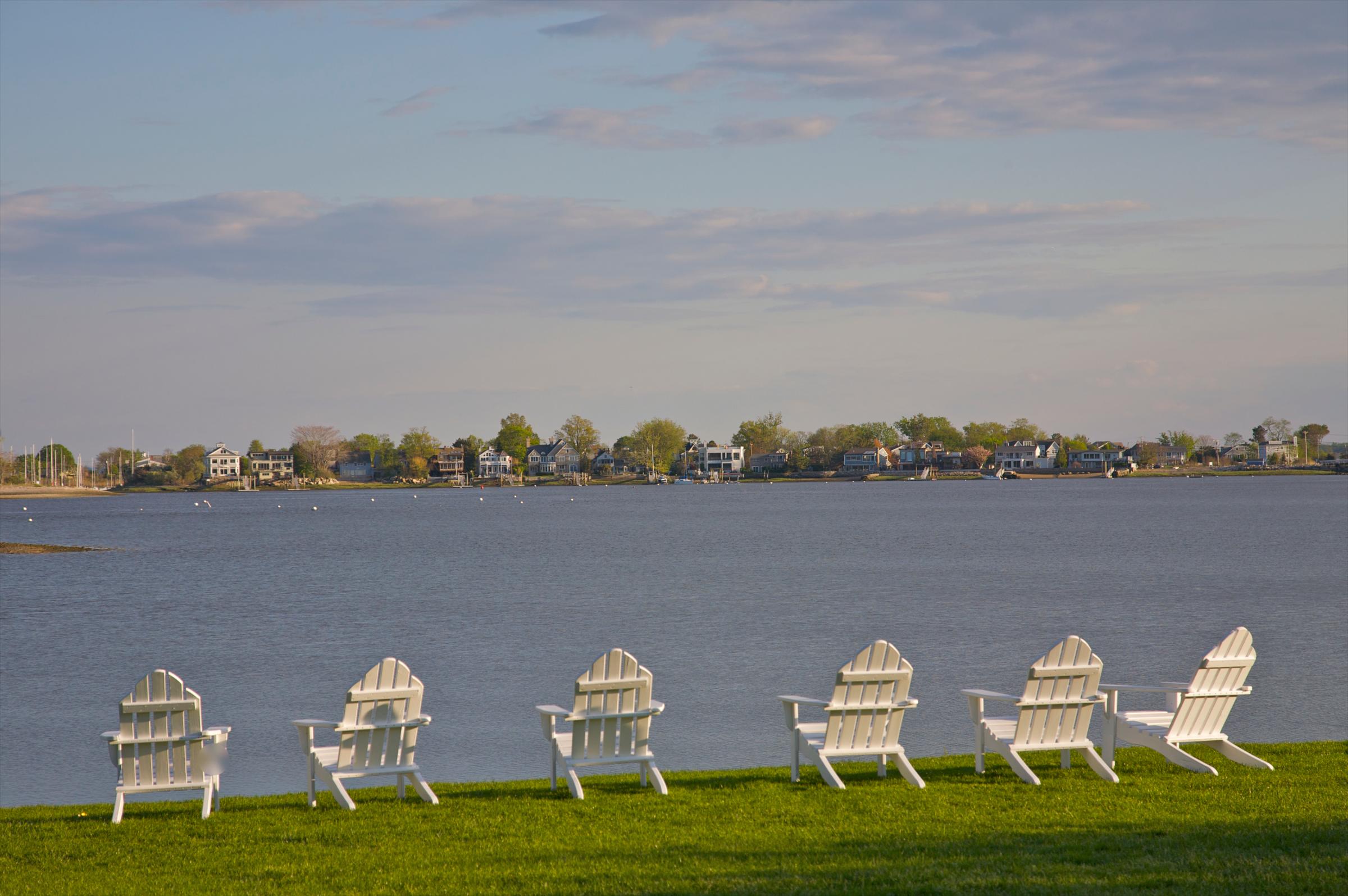 Six white chairs facing water and shoreline houses