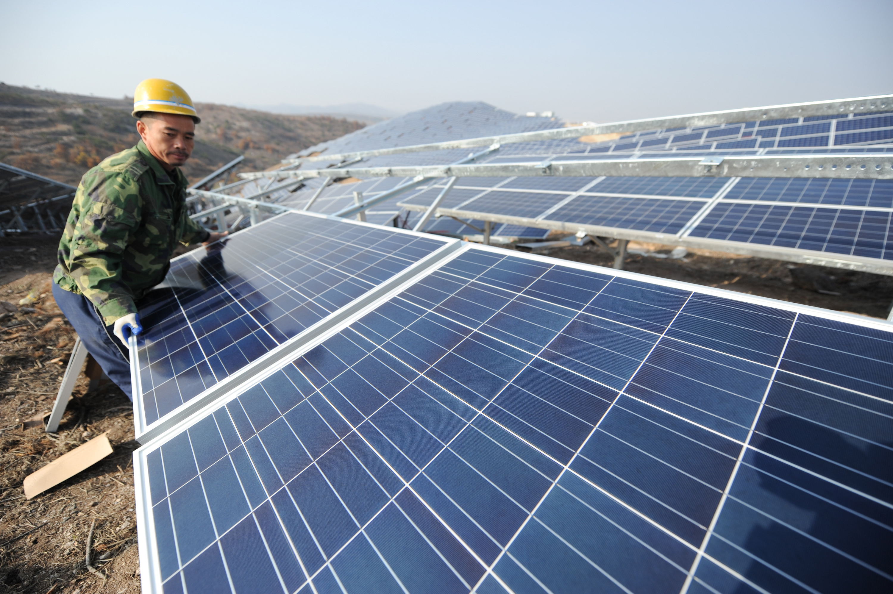 A worker installs polycrystalline silicon solar panels as terrestrial photovoltaic power project starts in 2015 in Yantai, Shandong Province of China. (VCG—Getty Images)