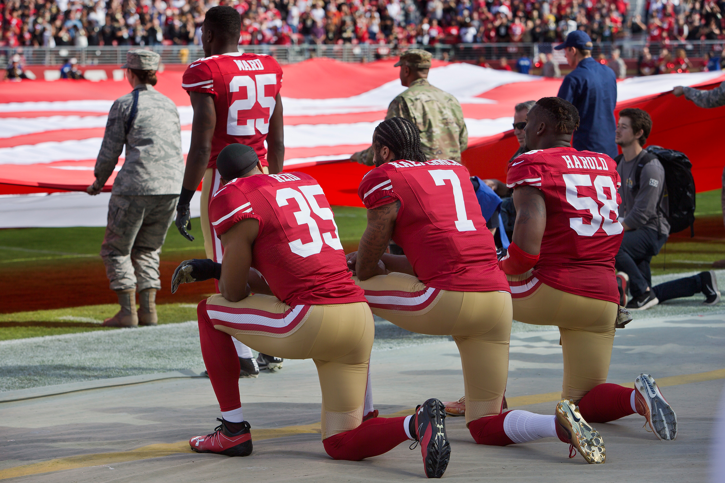 Quarterback Colin Kaepernick #7, safety Eric Reid #35, and linebacker Eli Harold #58 of the San Francisco 49ers kneel before a game against the New Orleans Saints with the U.S. flag unfurled in honor of the armed services on Nov. 6 2016 at Levi's Stadium in Santa Clara, Calif. (Brian Bahr—Getty Images)