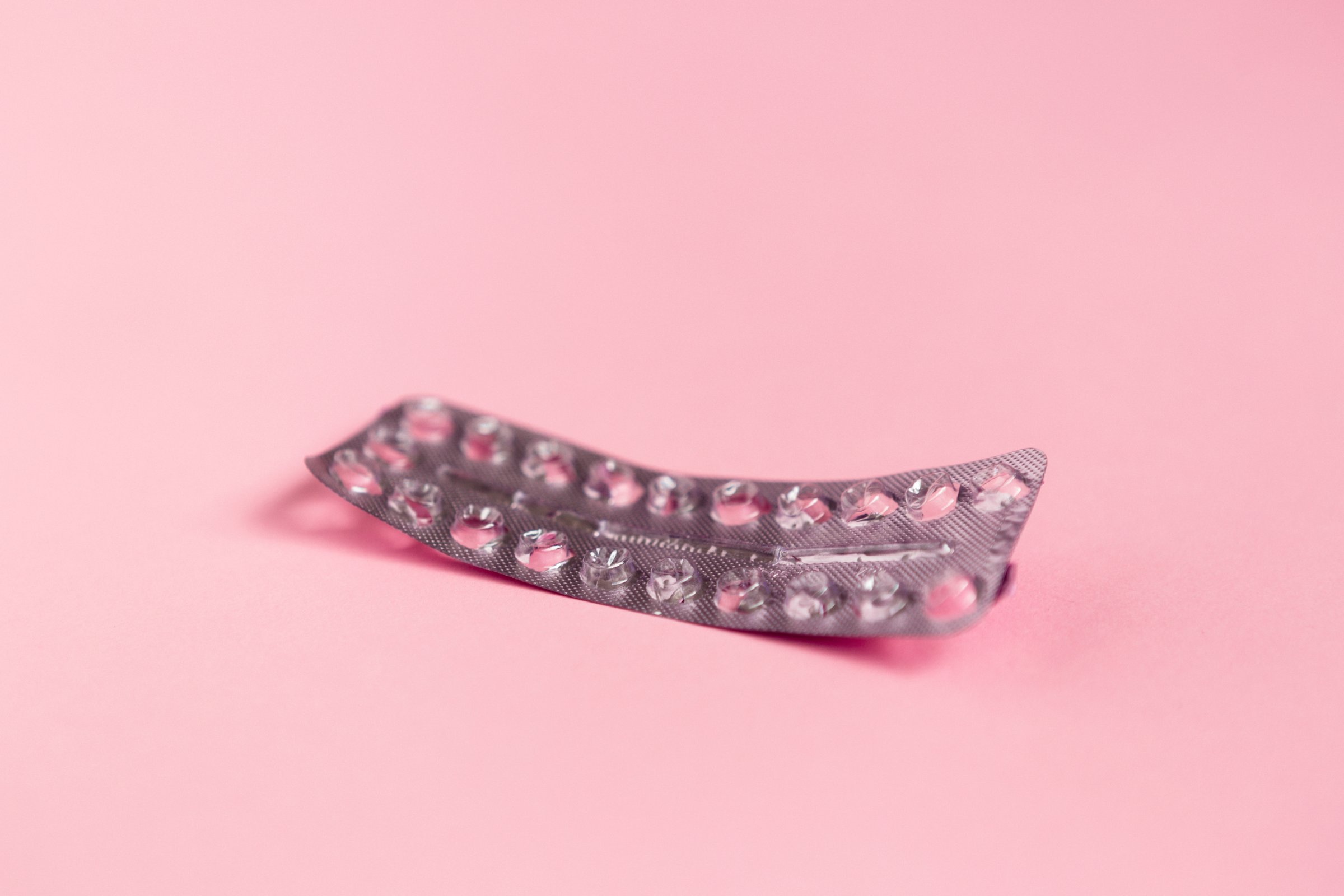 Empty strip of birth control pills on pink background.
