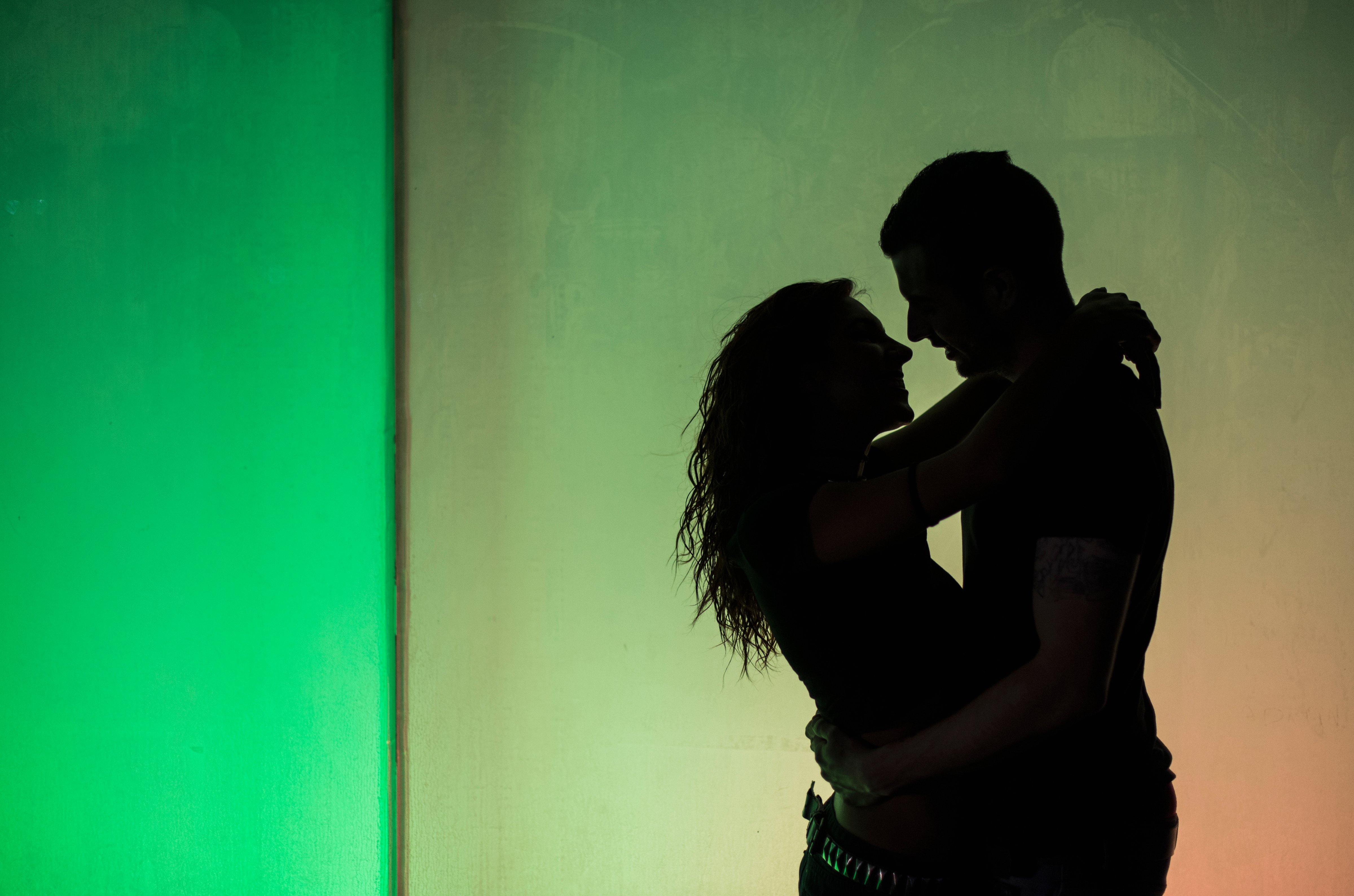 Silhouettes of young couple in love on a wall at greenish light