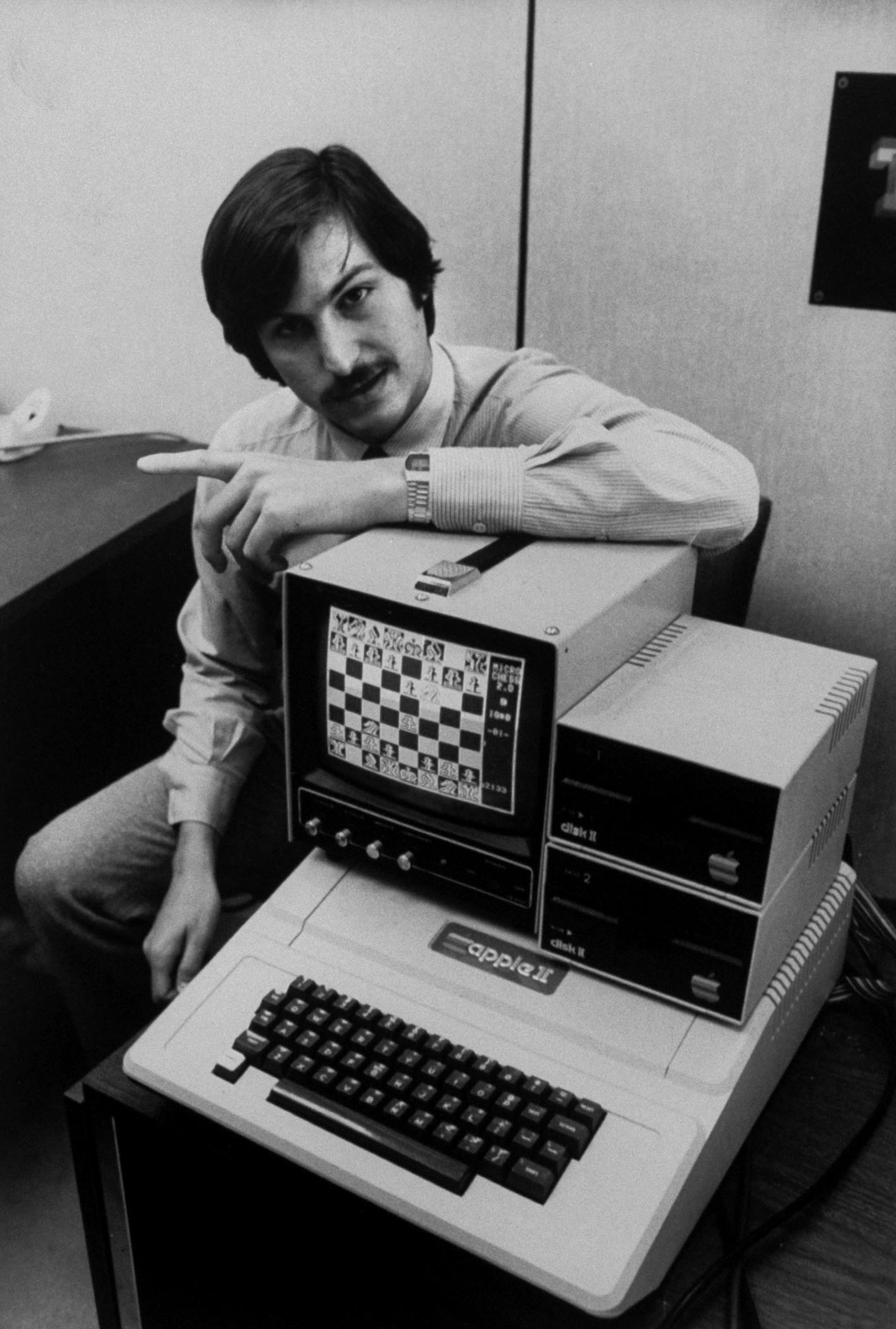 Steve Jobs with Apple II computer, with chess game displayed on screen.