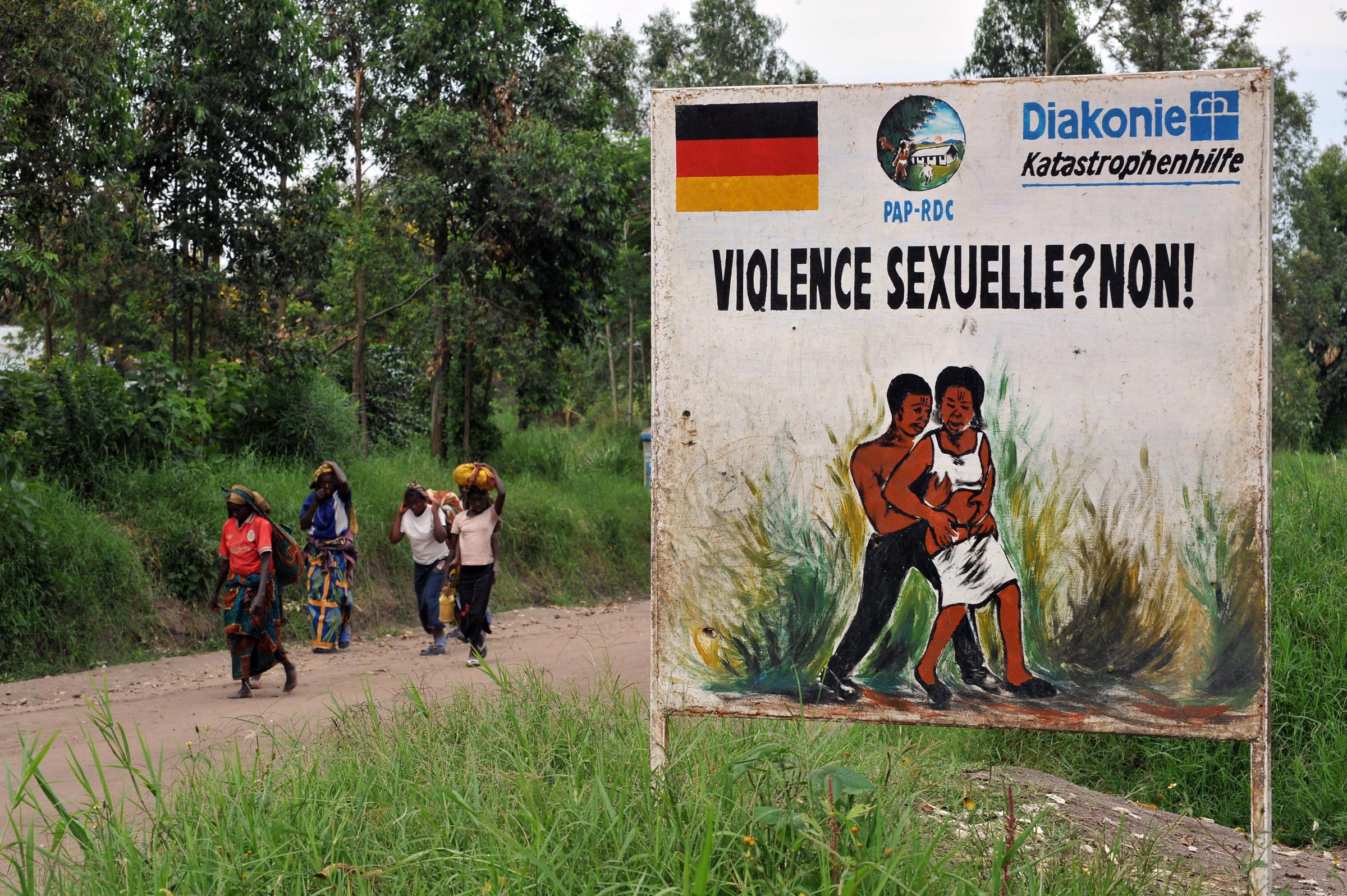 Congolese women walk past a sign opposin