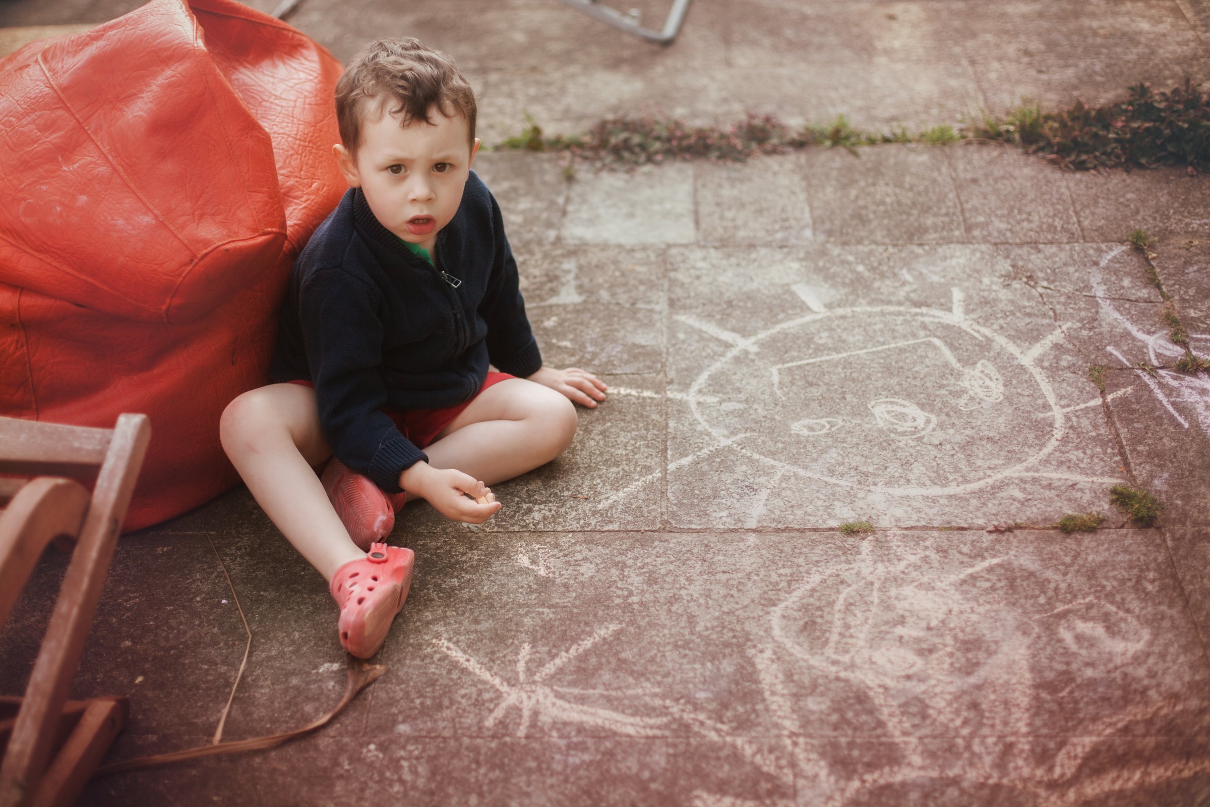 little boy (3) drawing  with chalk on the floor outdoors