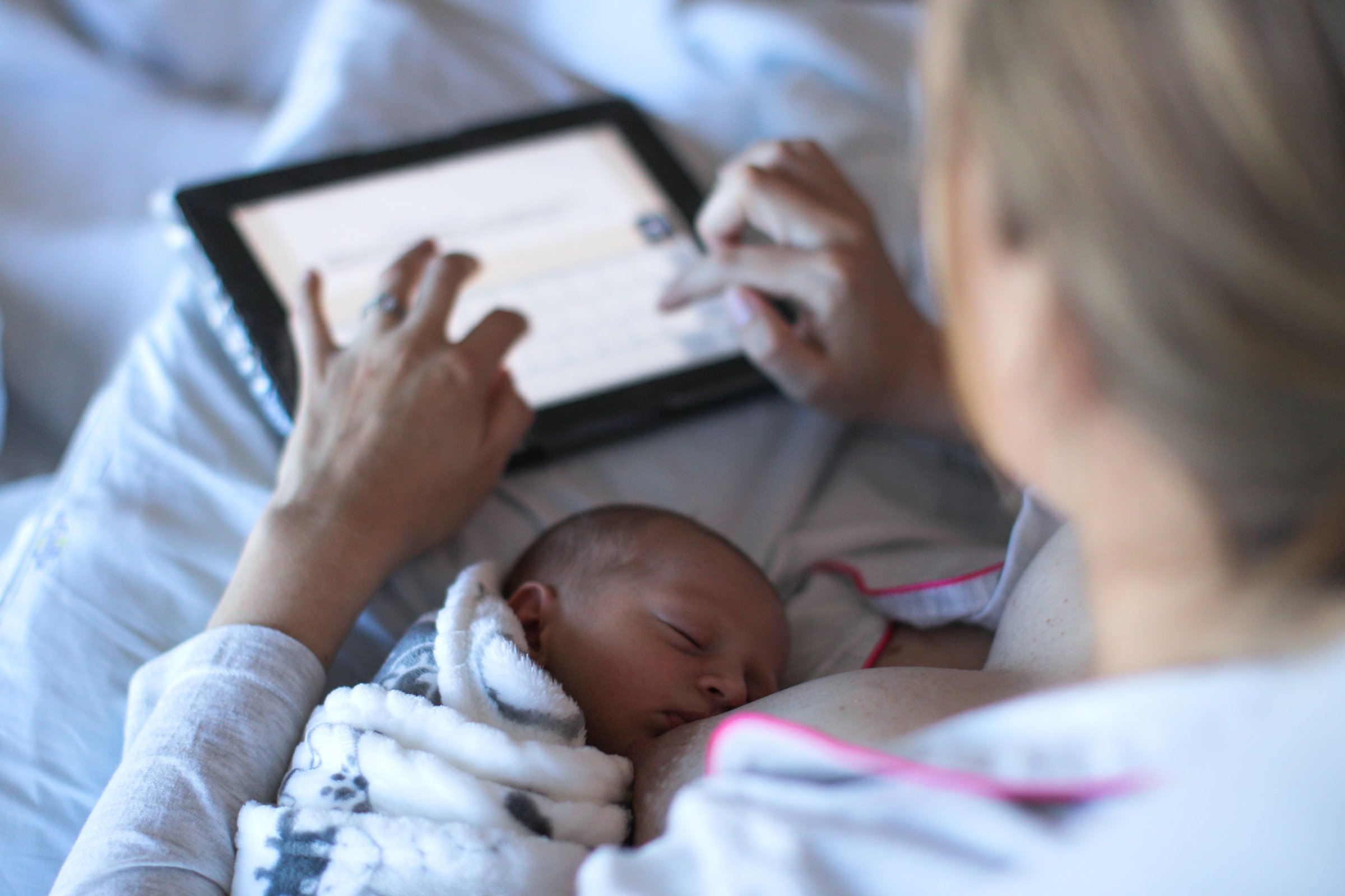 a Young woman fills in a revue of the hospital she gave birth in on a digital tablet while breastfeeding.