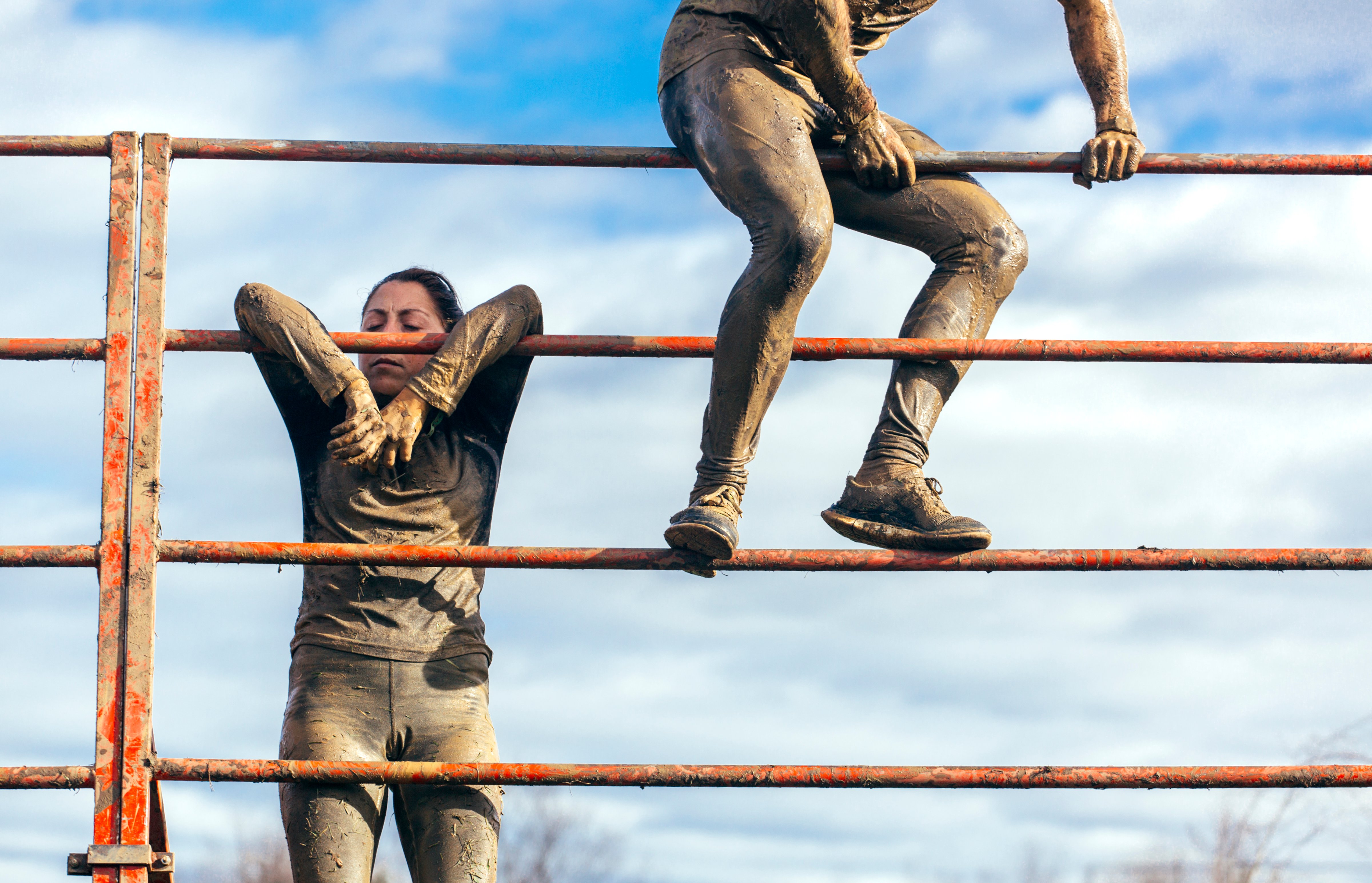 Participants in extreme obstacle race climbing over hurdle