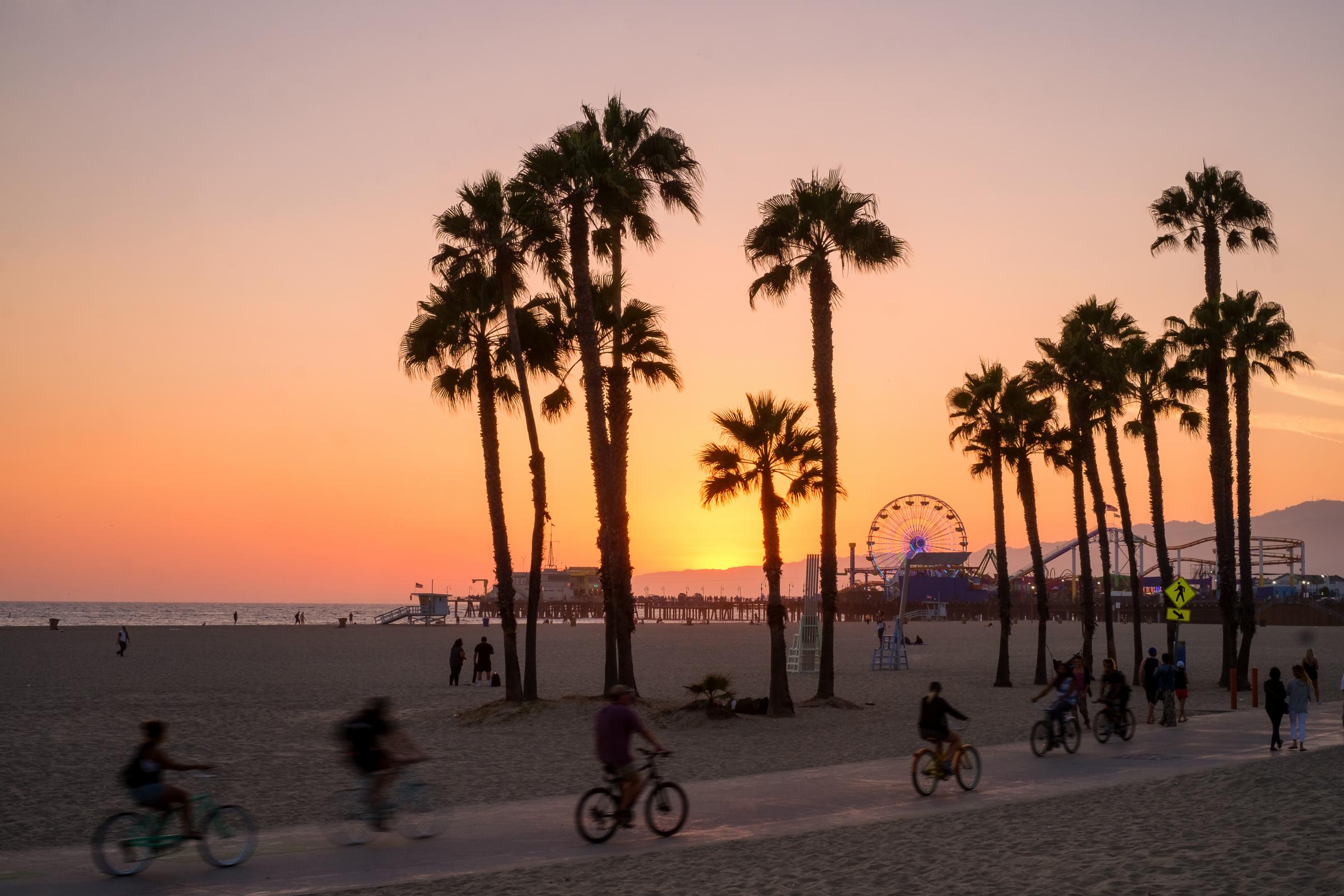 People ride bikes and walk along the beach at sunset in Santa Monica, California.