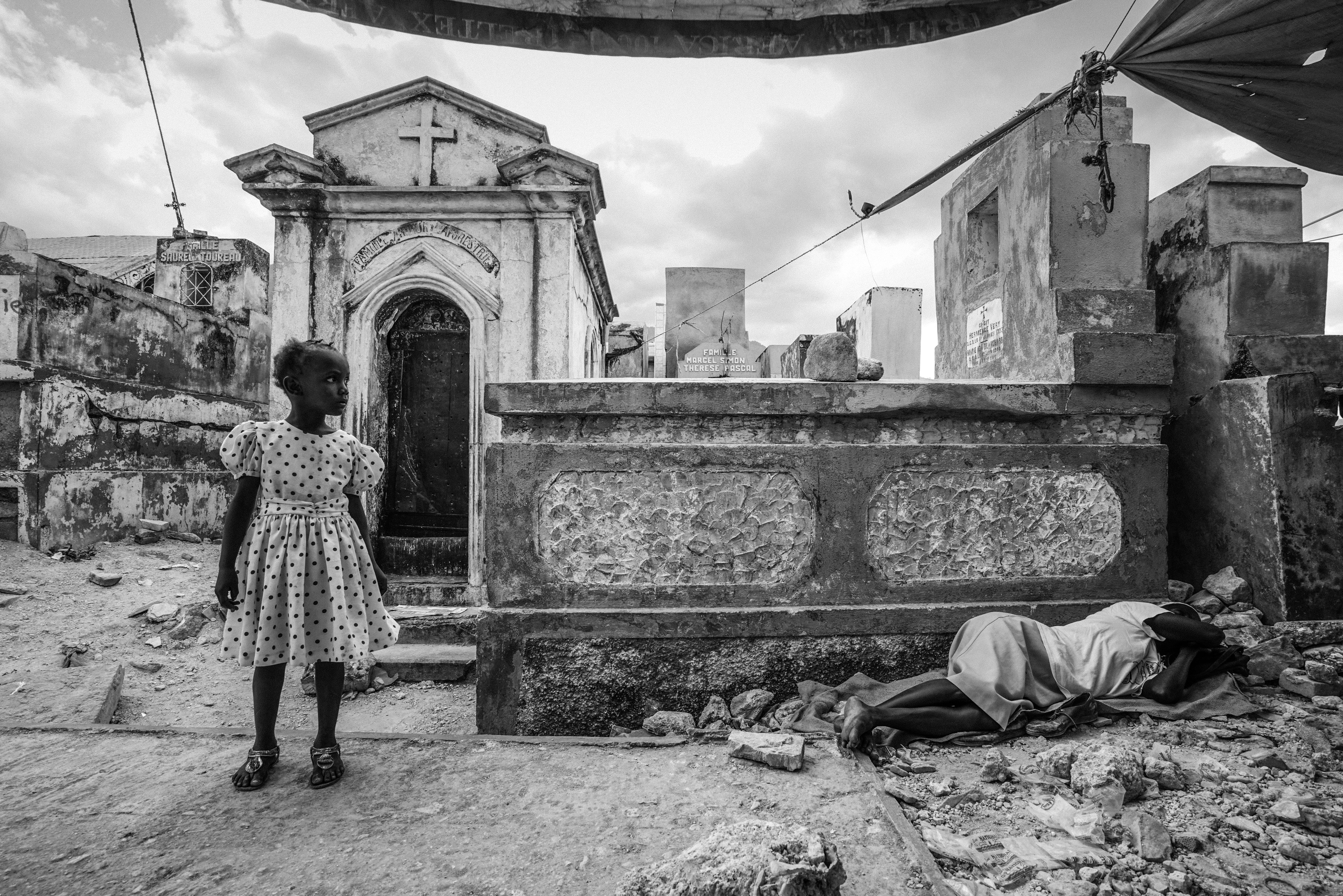 On the fifth anniversary of the devastating earthquake, a young child stands to the side of her mourning mother who lies weeping nearby in the Grand Cemetery of Port-Au-Prince, Haiti, Jan. 12, 2015. (Giles Clarke—Getty Images)