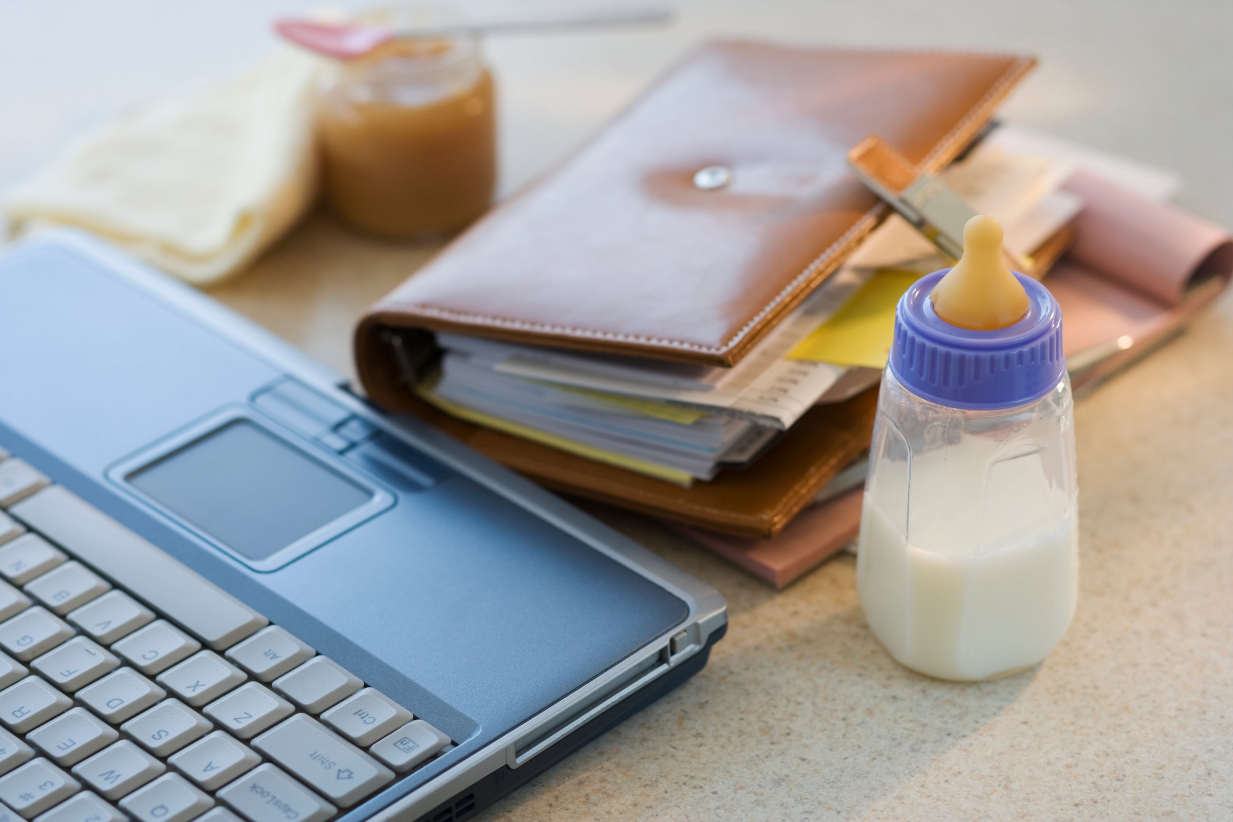 Laptop, planner and baby bottle on table