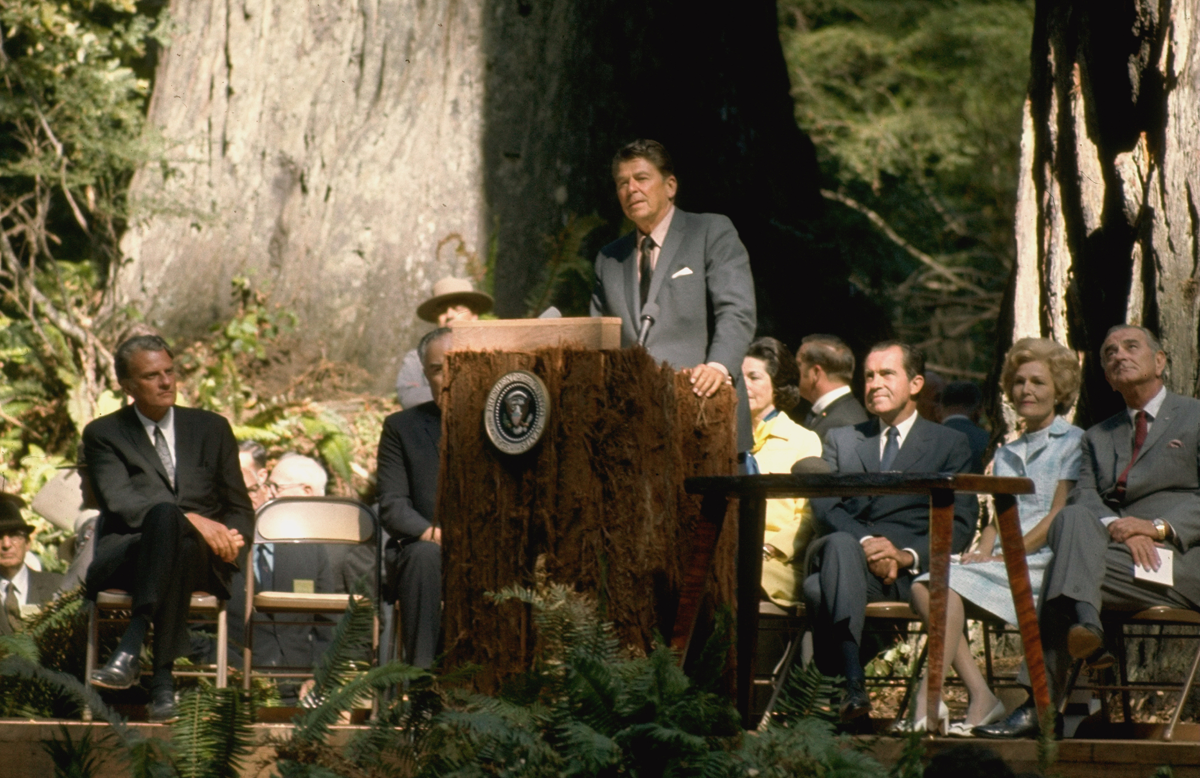 California Governor Ronald Reagan speaking while standing at podium as Reverend Billy Graham, Richard Nixon and wife Pat and Lyndon Johnson look on at Redwood National Park. (Julian Wasser—The LIFE Images Collection/Getty Images)