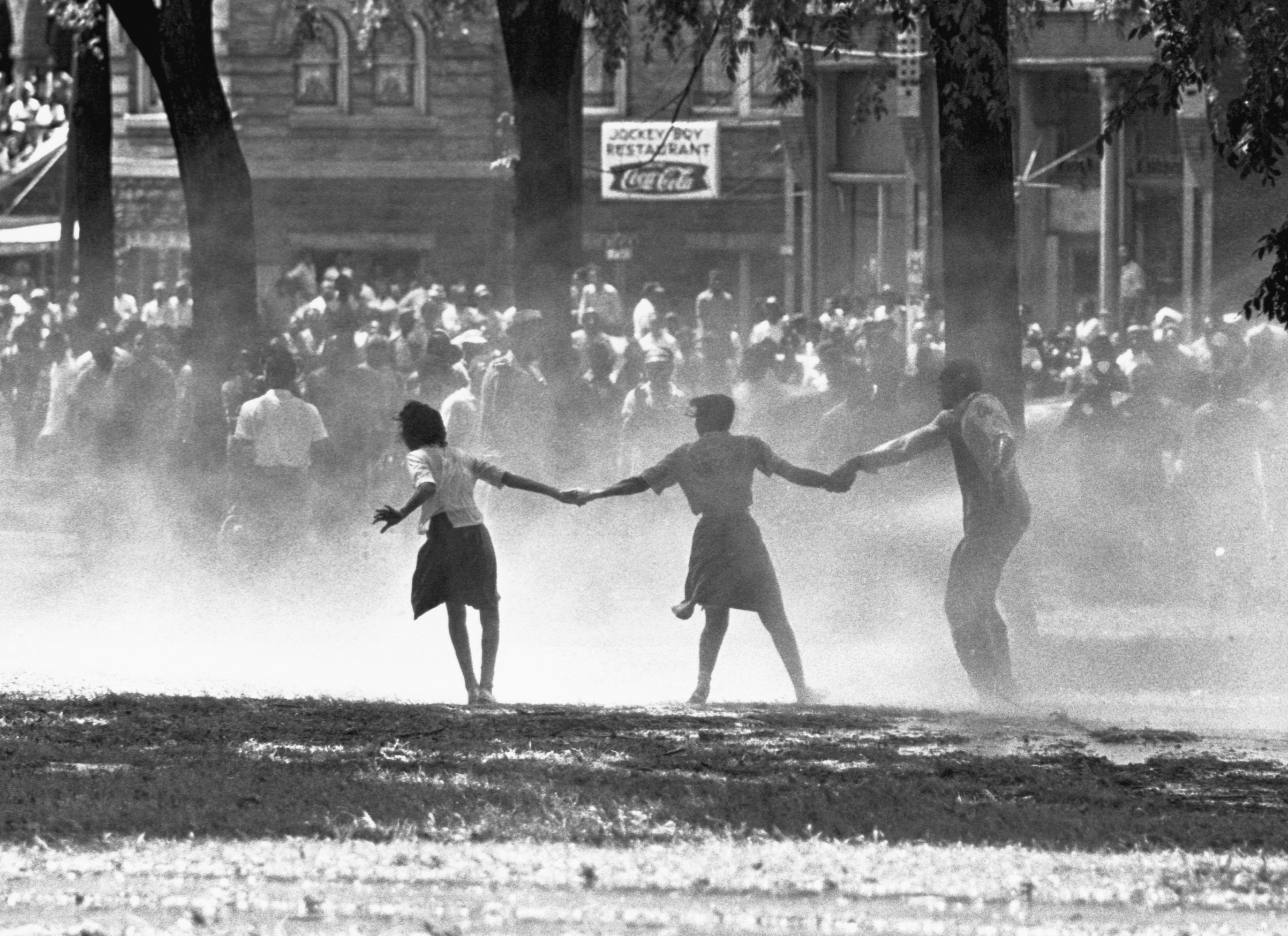 Three demonstrators join hands to build strength against the force of water sprayed by riot police in Birmingham, Alabama, during a protest of segregation practices in May of 1963. (Bettmann / Getty Images)