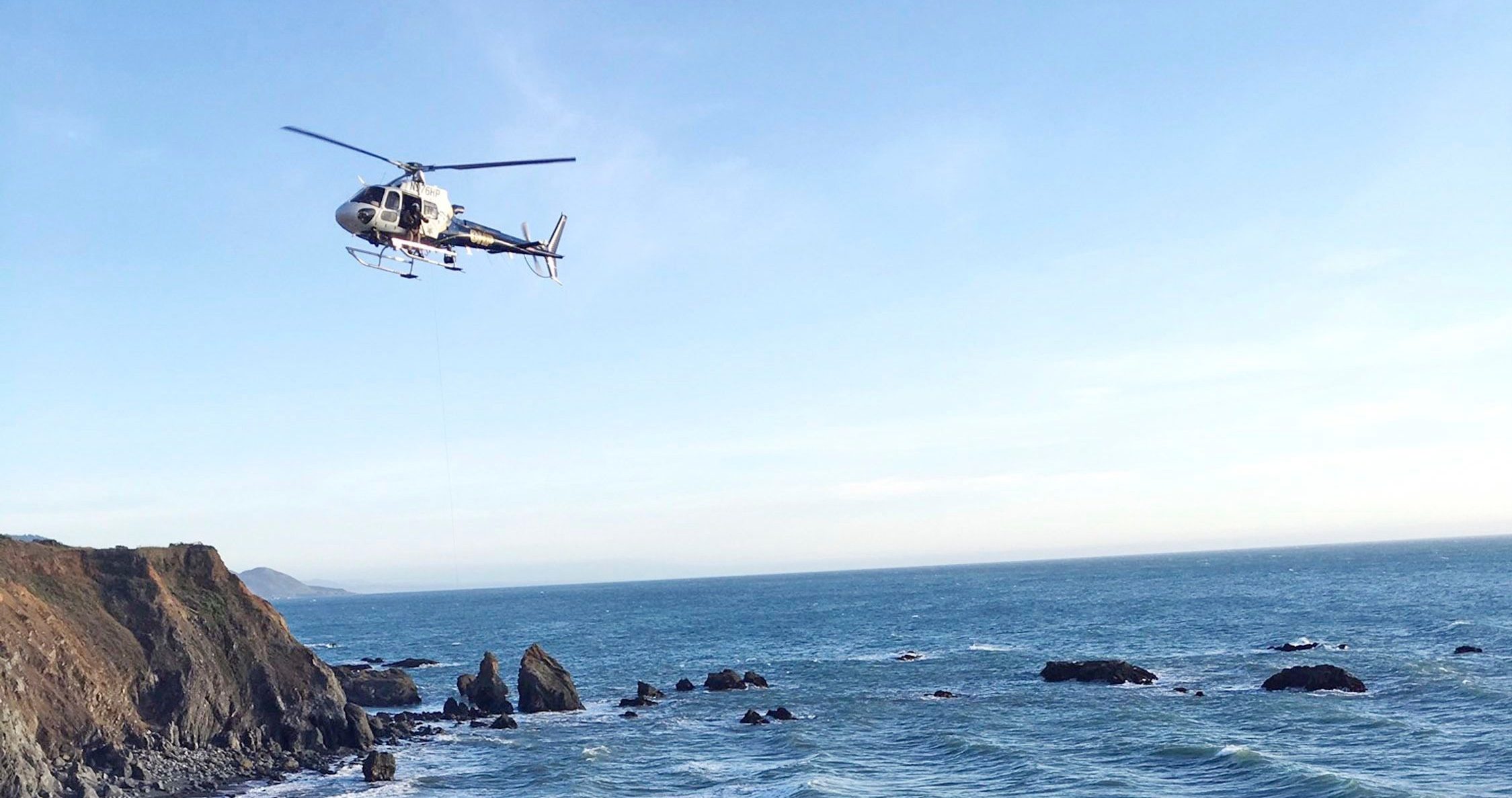 A helicopter hovers over steep coastal cliffs, near Mendocino, Calif., where a vehicle, visible at lower right, plunged about 100 feet off a cliff along Highway 1, killing five passengers. (California Highway Patrol —AP)