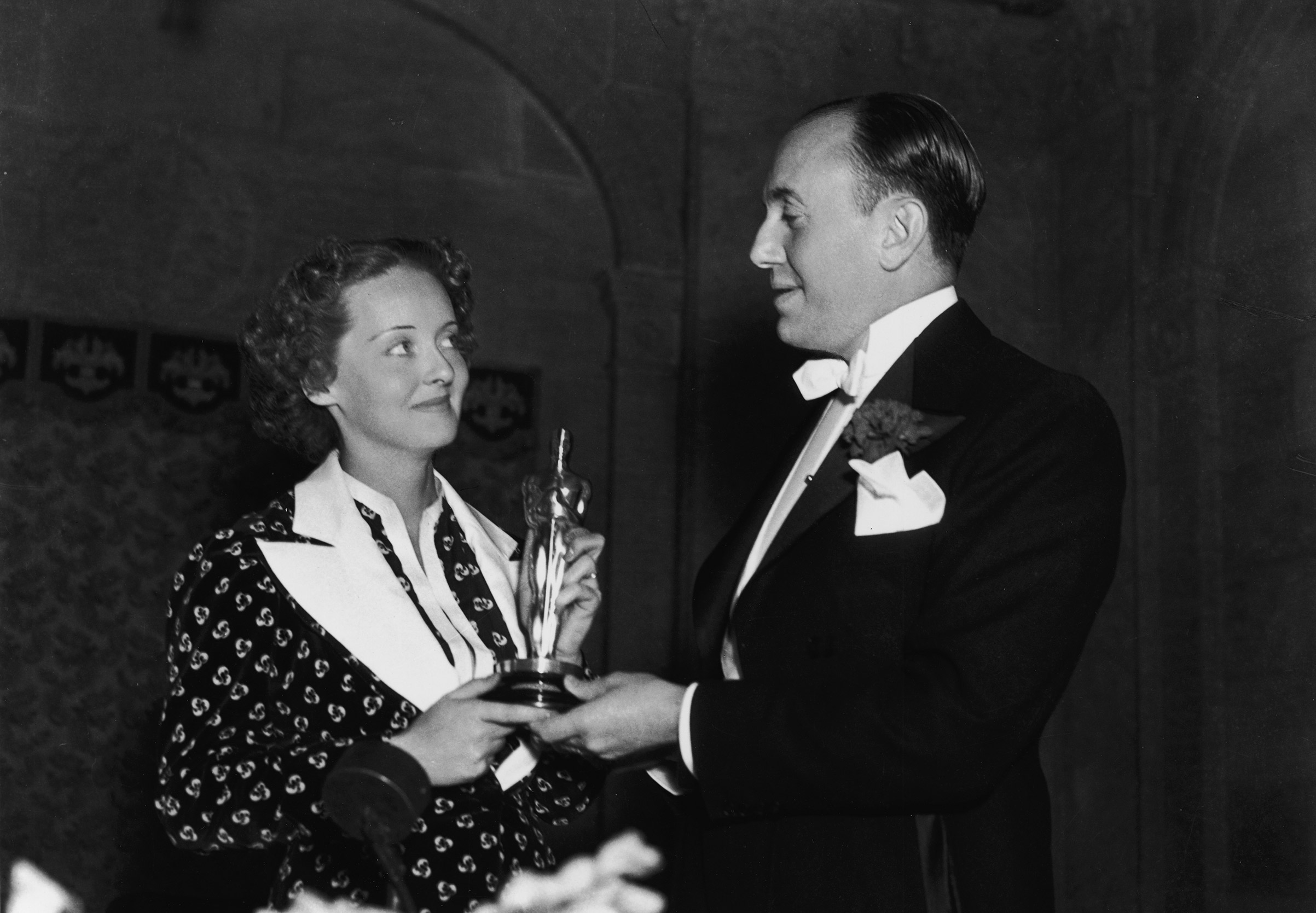 Actor Bette Davis and producer Jack Warner, one of the founders of Warner Bros. Pictures, hold Davis's Oscar for Best Actress for <i>Dangerous</i> at the Biltmore Hotel in Los Angeles, California, on March 5, 1936. (Hulton Archive—Getty Images)