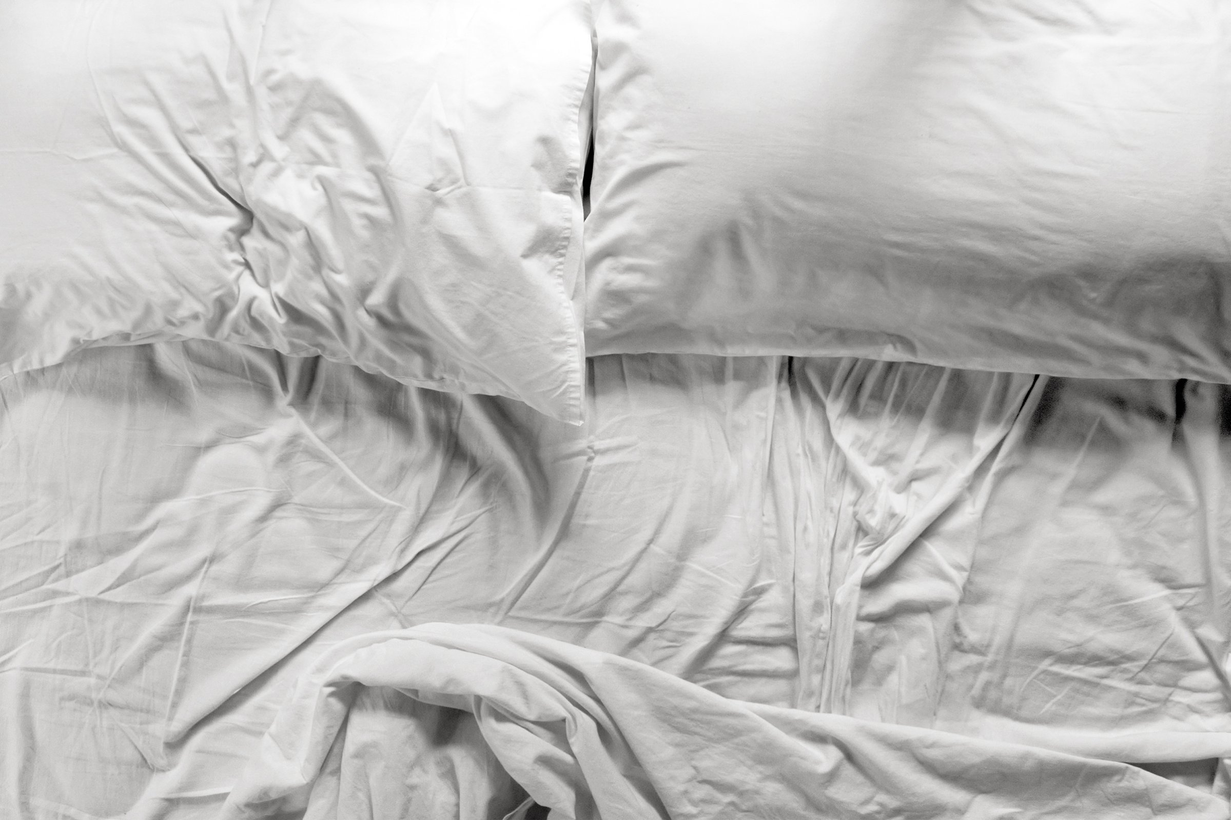 Unmade bed in a bedroom with two pillows and crumpled bed sheet