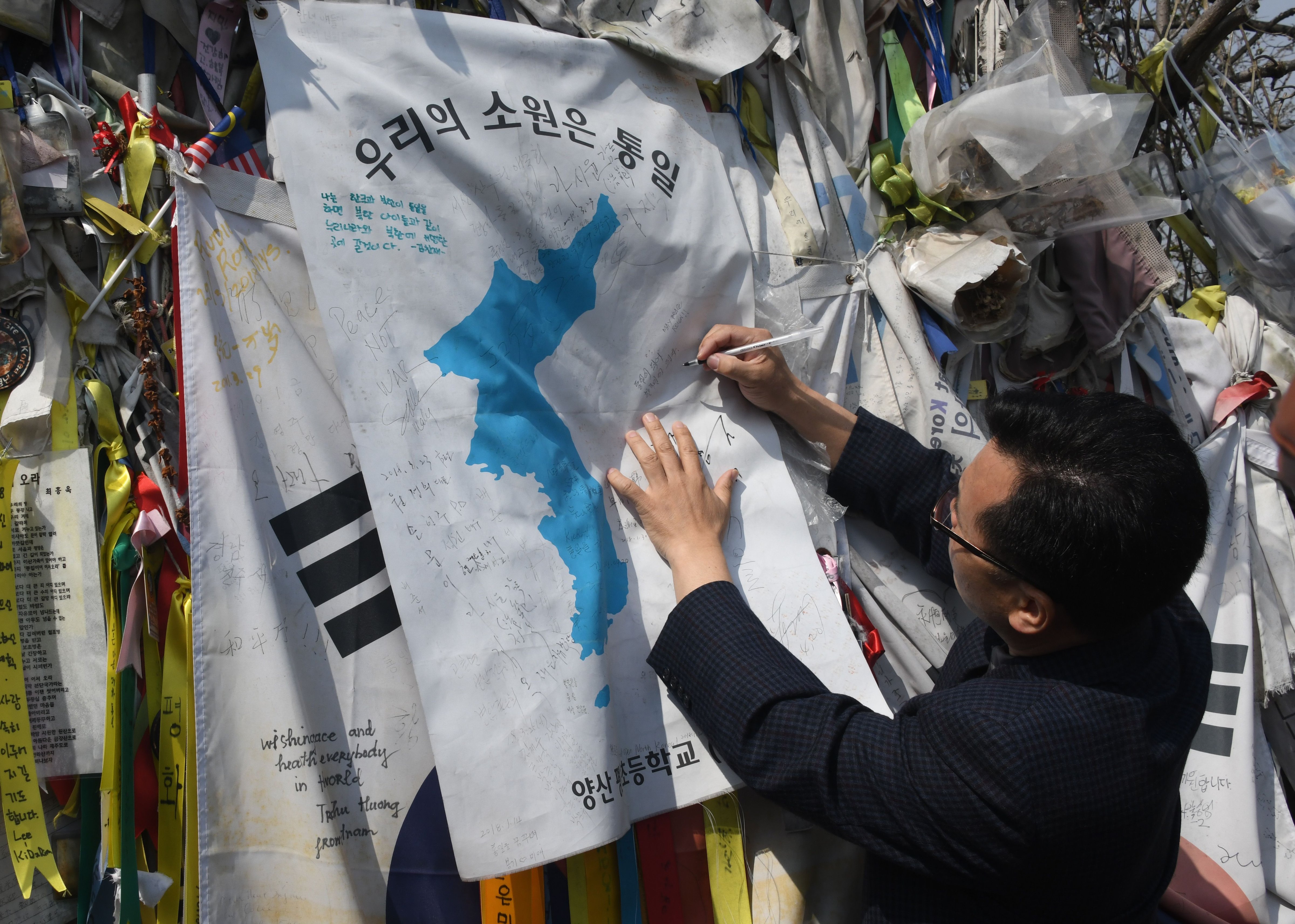 A man writes an inscription on a "Unification flag" hanging at a military fence at Imjingak peace park in Paju near the demilitarized zone dividing the two Koreas on April 26, 2018 ahead of the upcoming inter-Korea summit. (Jung Yeon-Je—AFP/Getty Images)