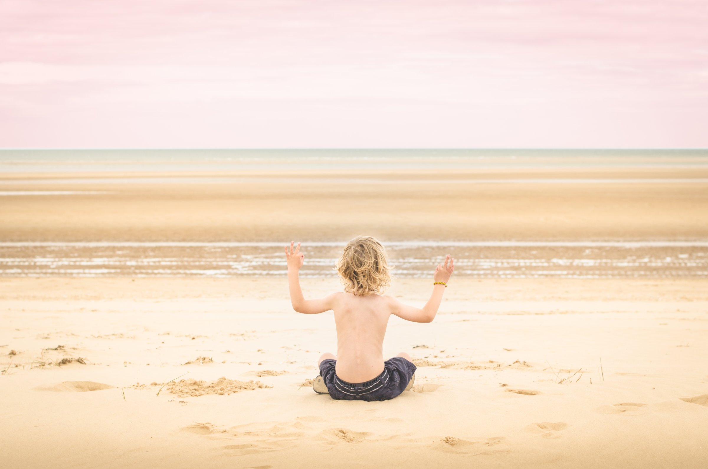 Boy sitting on beach, arms raised