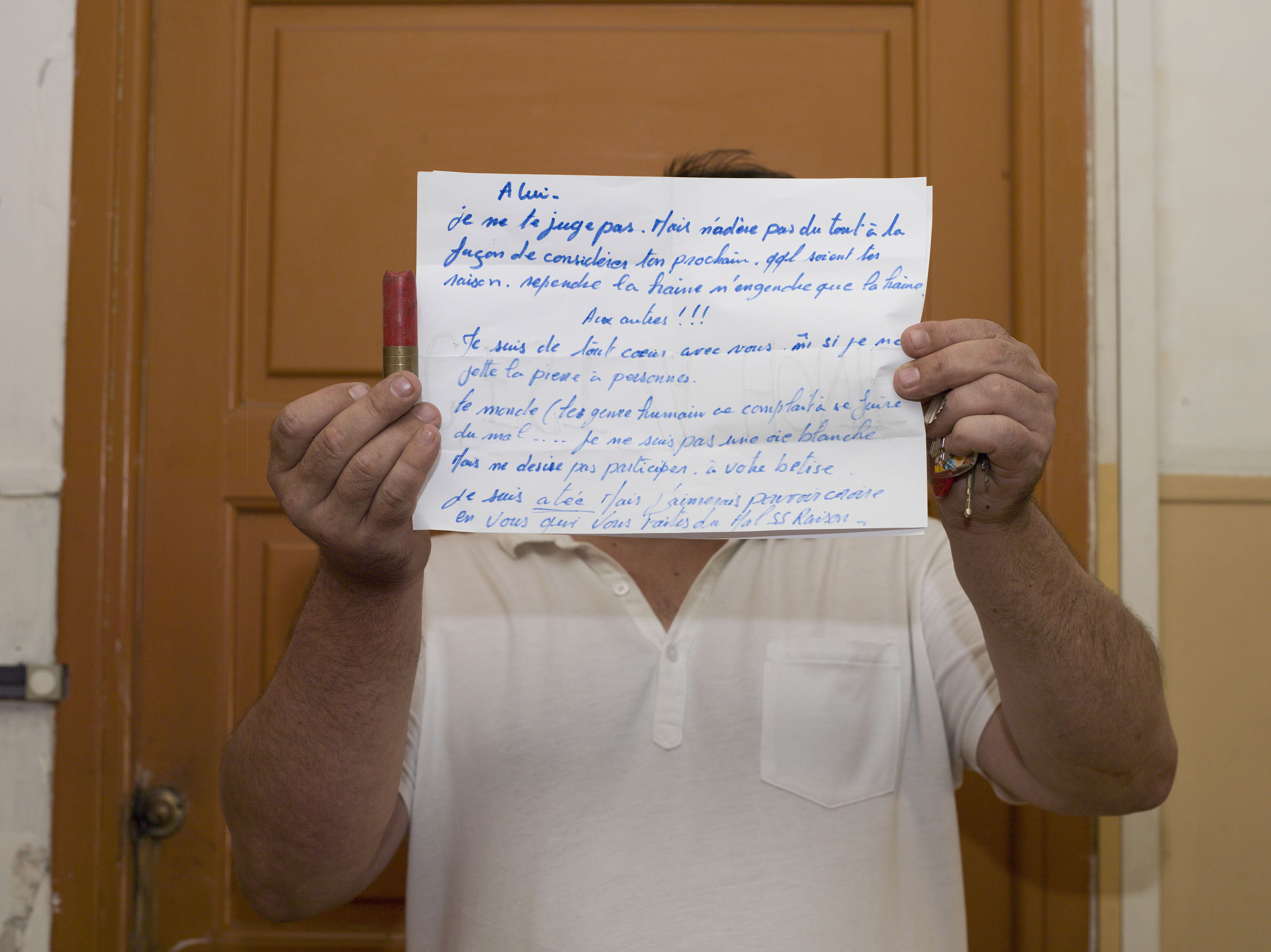 A neighbor, who didn't want to be identified holds a sign, in front of Mohamed Lahouaiej Bouhlel's doorway. Bouhlel was the driver of a truck that plowed into a crowd on the waterfront in Nice, France, killing 84 people. Holding a bullet shell from the police's forced entrance, he holds a sign that reads: "For him: I do not blame you. But I do not join you at all in the way you consider your neighbor. Regardless of your reason. Spilled hatred only begets hatred. For the others: I'm with you even if I do not throw stones on anybody. The world keeps hurting itself. I am not a white goose but I do not desire to participate in your foolishness." 2016. (Alessandra Sanguinetti—Magnum Photos)
