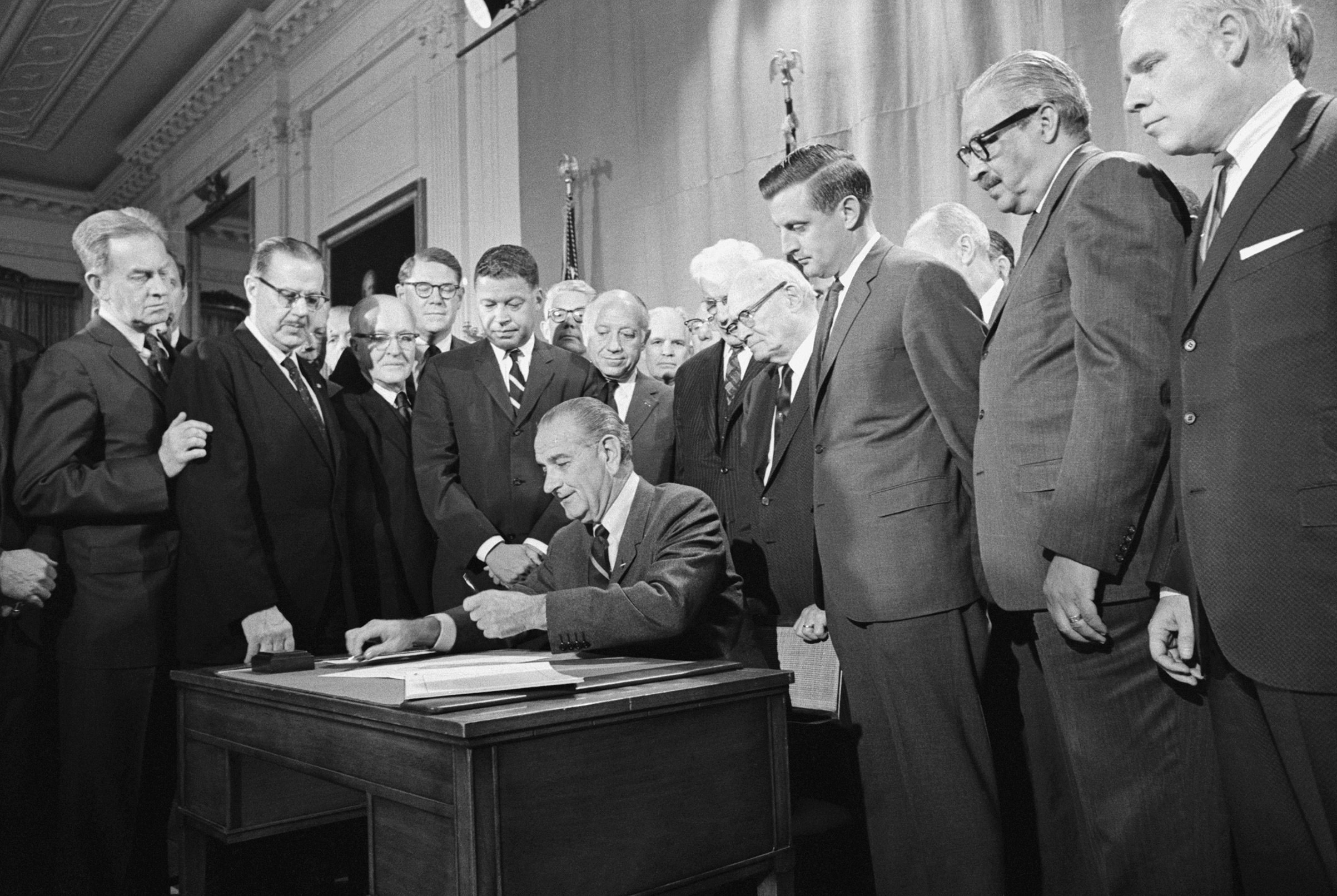 The Fair Housing Act's co-sponsors,  Democratic Senator from Minnesota Walter Mondale (third from right) and Republican Senator from Massachusetts Edward Brooke (fourth from the left in the striped tie), watch President Lyndon B. Johnson sign the civil rights bill into law on April 11, 1968. (Bettmann—Getty Images)