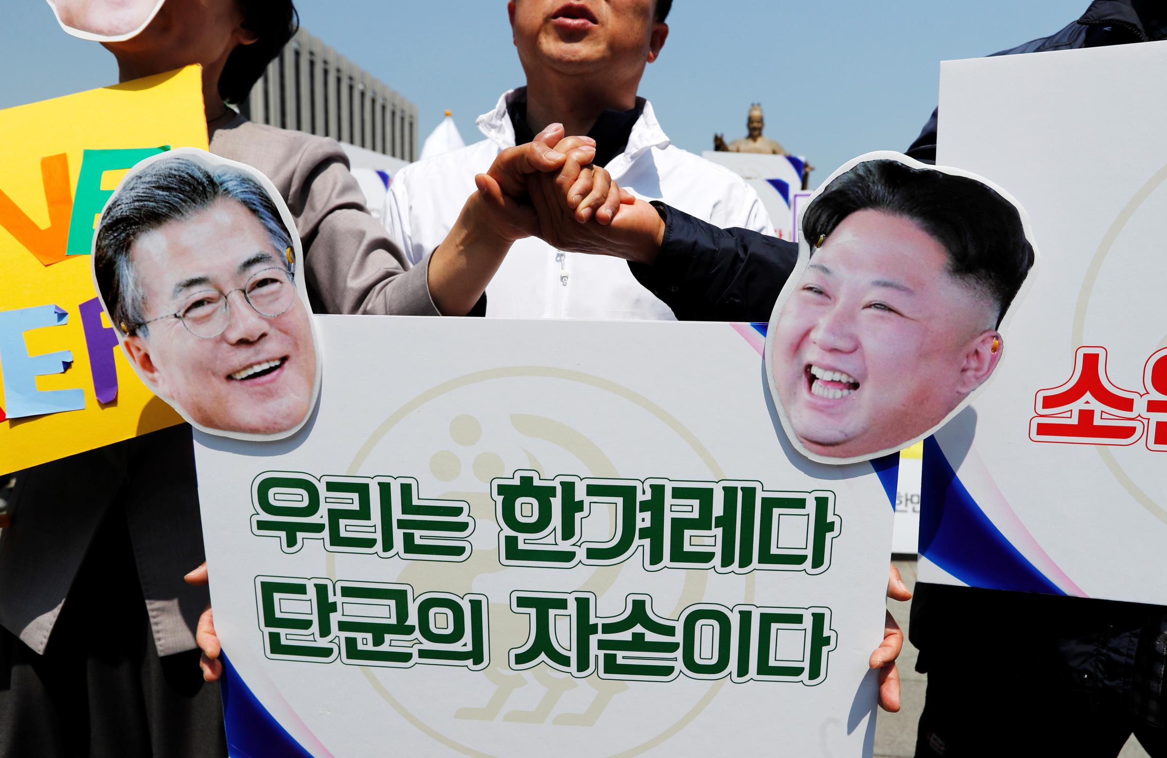 People hold hands behind a sign with cutouts of South Korea's President Moon Jae-in and North Korea's leader Kim Jong Un during a pro-unification rally ahead of the upcoming summit between North and South Korea in Seoul