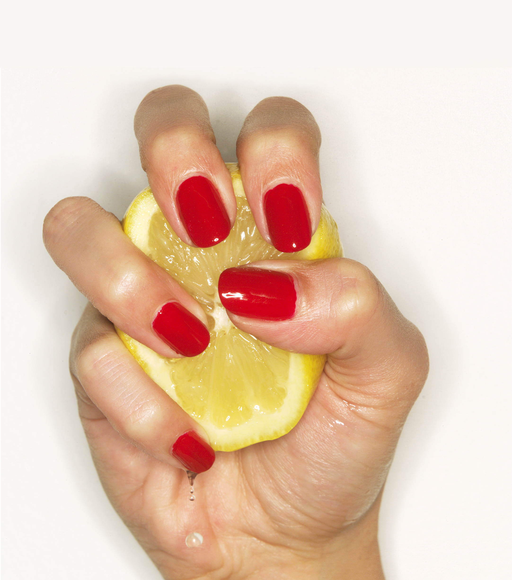 Hand of woman with red nail polish squeezing lemon