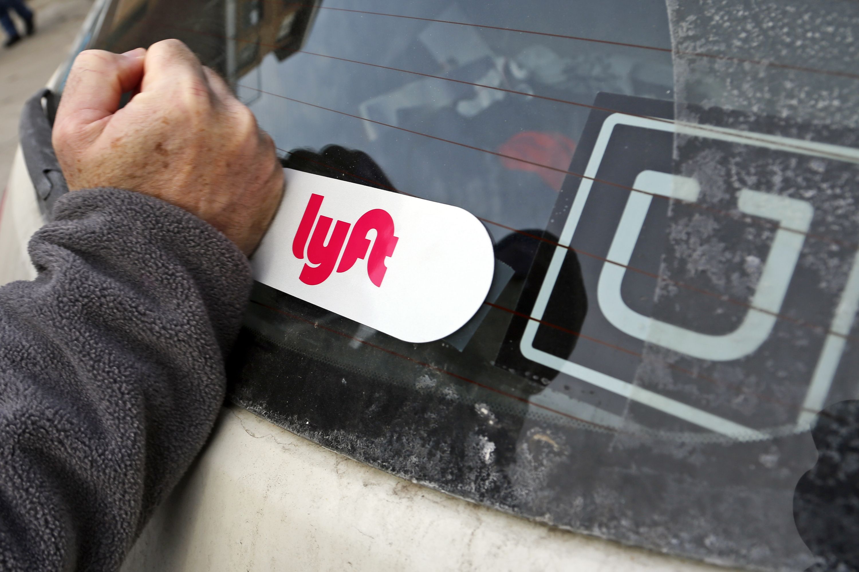 This is a Lyft logo being installed on a Lyft driver's car who also drives for Uber on in Pittsburgh, January 31, 2018. (Gene J. Puskar/AP/REX—Shutterstock)